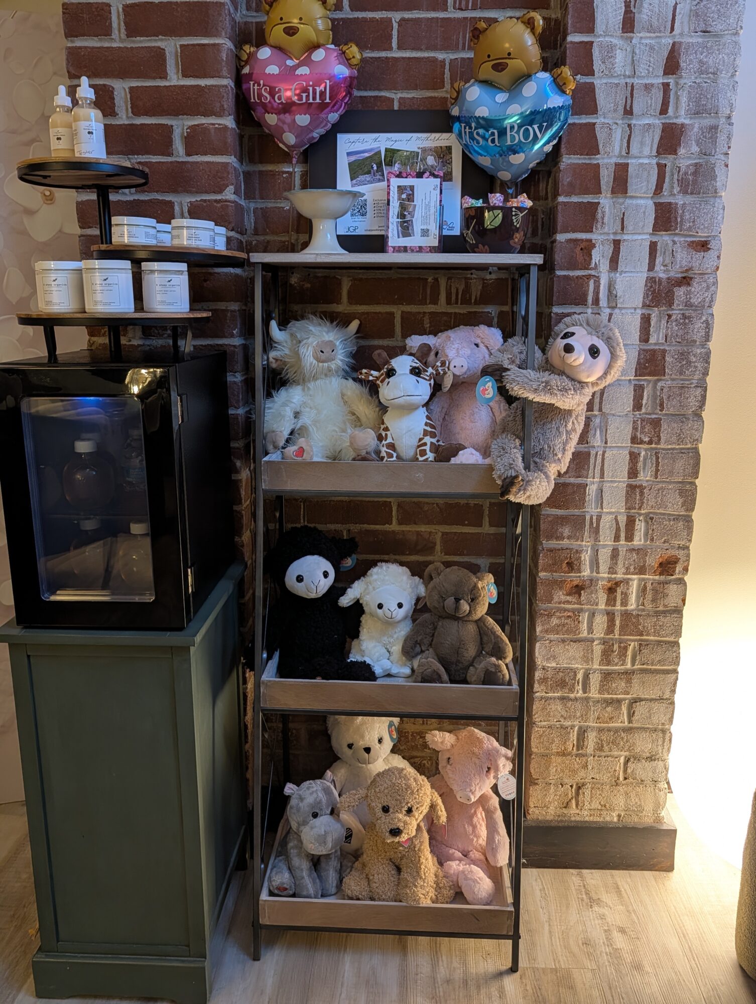 Wooden shelf with stuffed animals, balloons, and decorative items against a brick wall, on a wooden floor.
