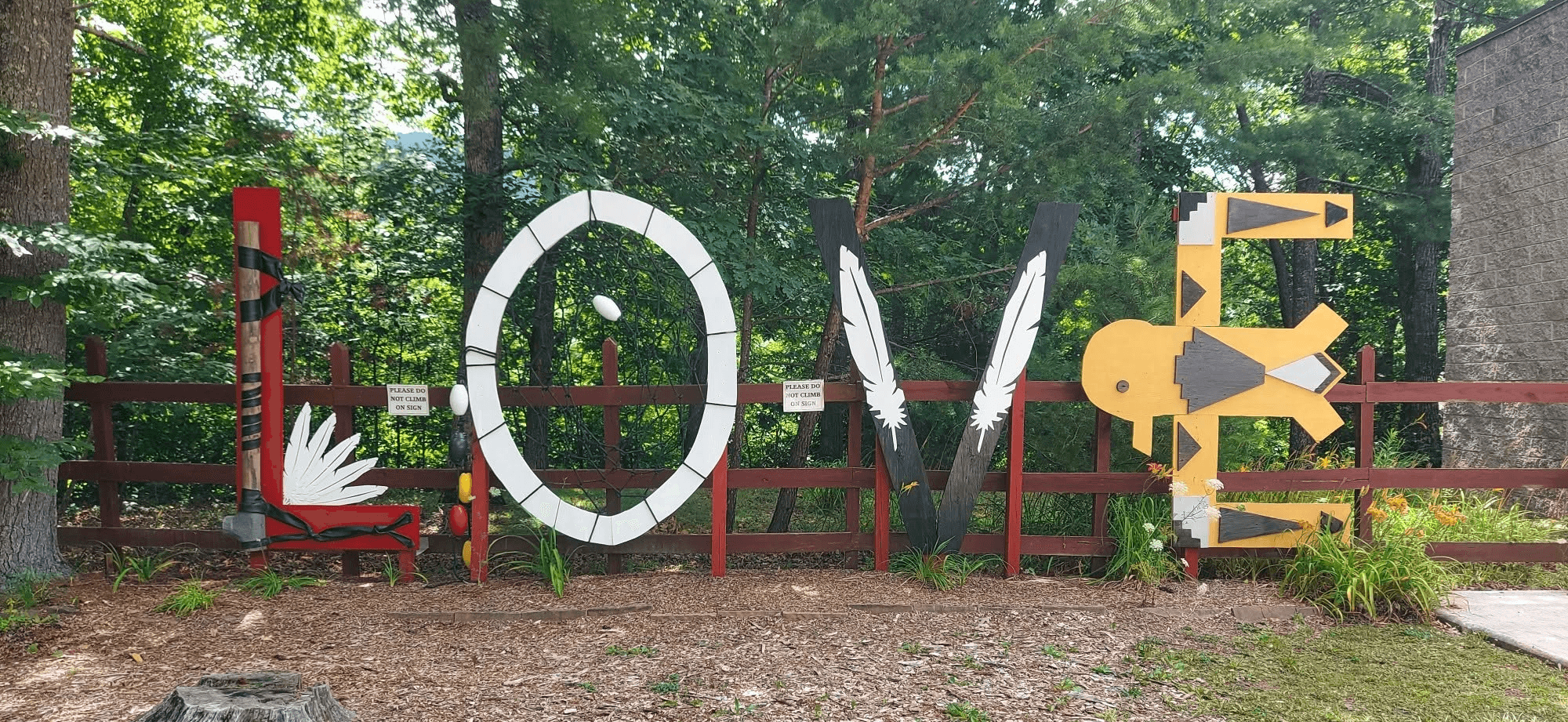 Colorful outdoor display spelling 'HOME' with decorative elements, set against a wooded background with a red fence.