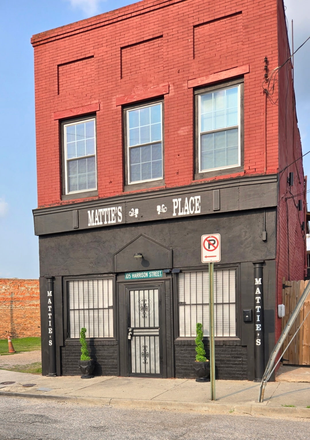 Three-story building with a red brick upper floor and a black storefront on the ground level, featuring large windows and a door.