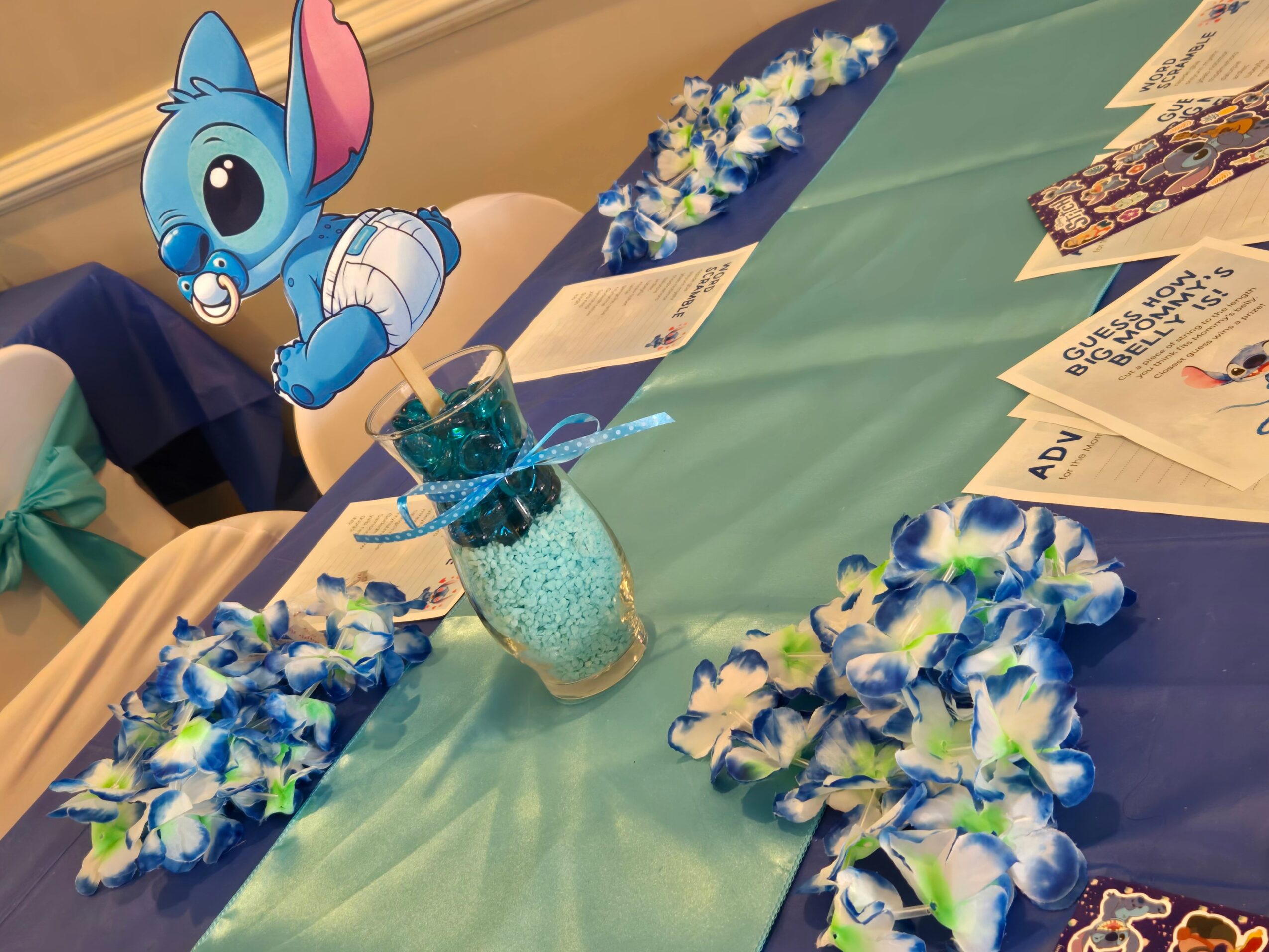 Table decorated with blue, white, and green flowers, a glass jar with blue beads, and cartoon character cutouts.