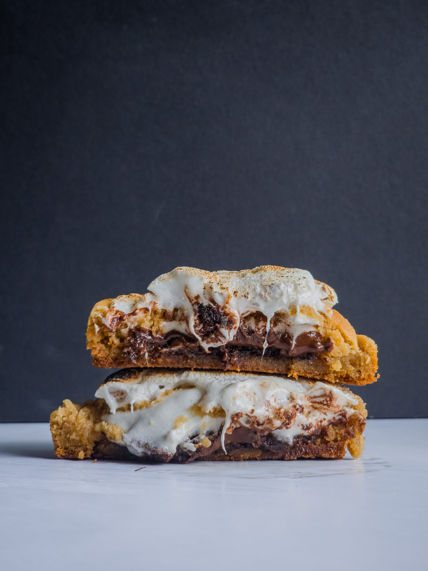 Two stacked dessert bars with melted marshmallow and chocolate, on a white surface against a dark background.