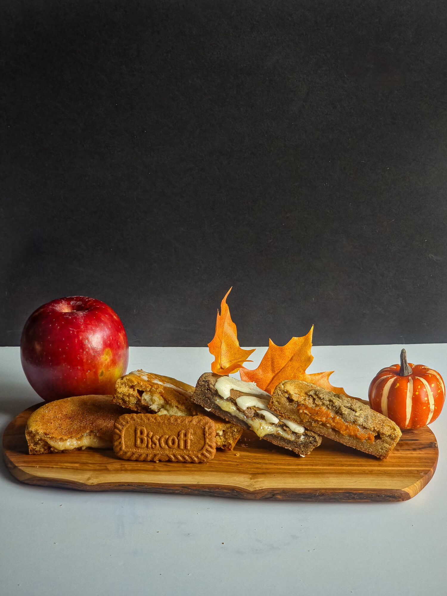 A wooden tray with an apple, biscuits, and slices of bread topped with leaves, on a black and white background.