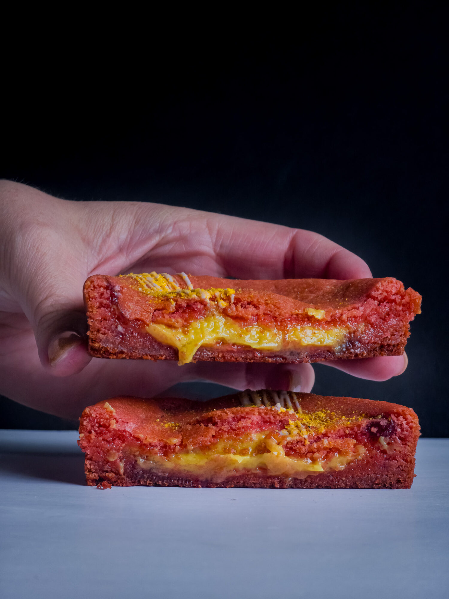 Hand holding a slice of layered, cheesy, and saucy baked dish with a crispy crust, placed on a white surface.