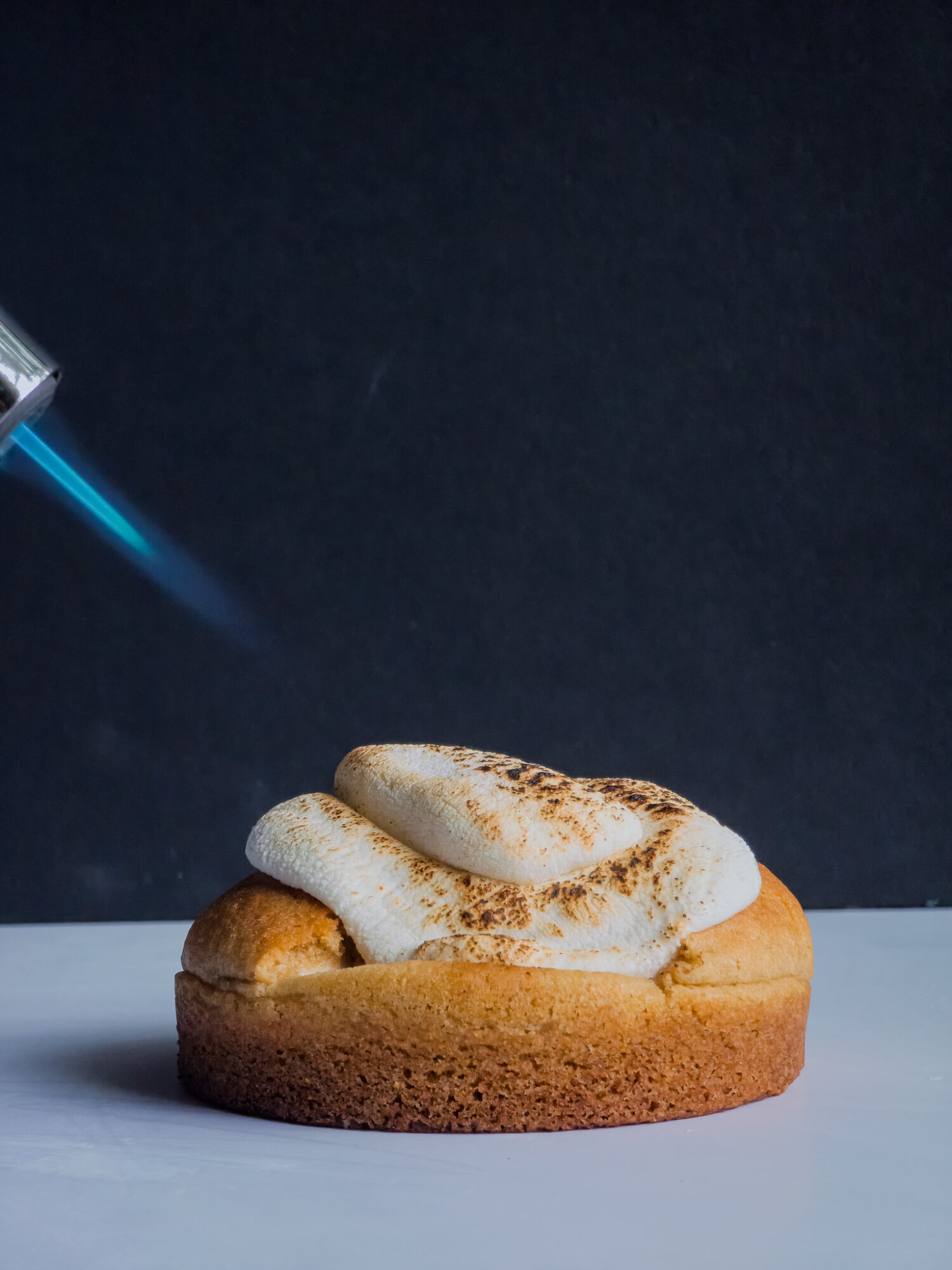 A dessert with a round base topped with whipped cream and a dusting of cocoa powder, against a dark background.
