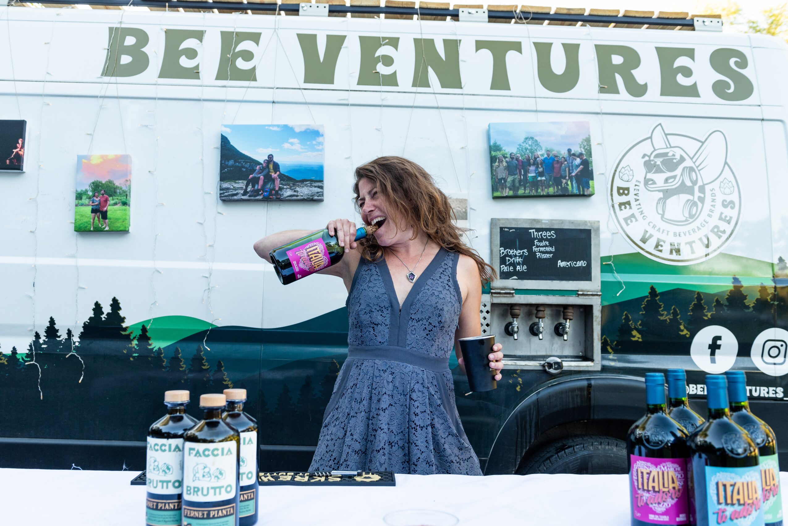 Woman in blue dress smiling and drinking from a bottle in front of a Bee Ventures vehicle with photos and logo.