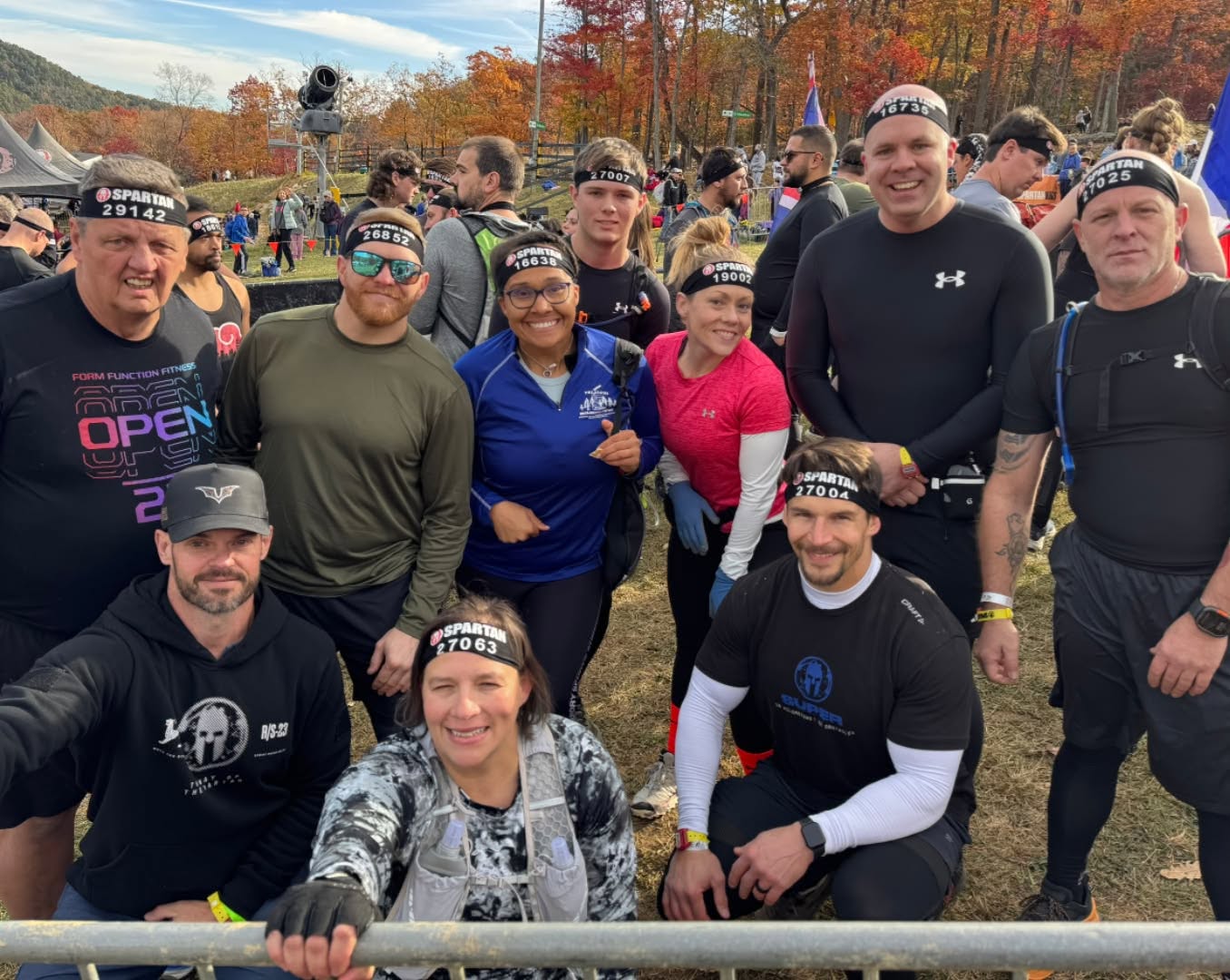 Group of people outdoors, some wearing athletic clothing and headbands, smiling for a photo during a race or event.