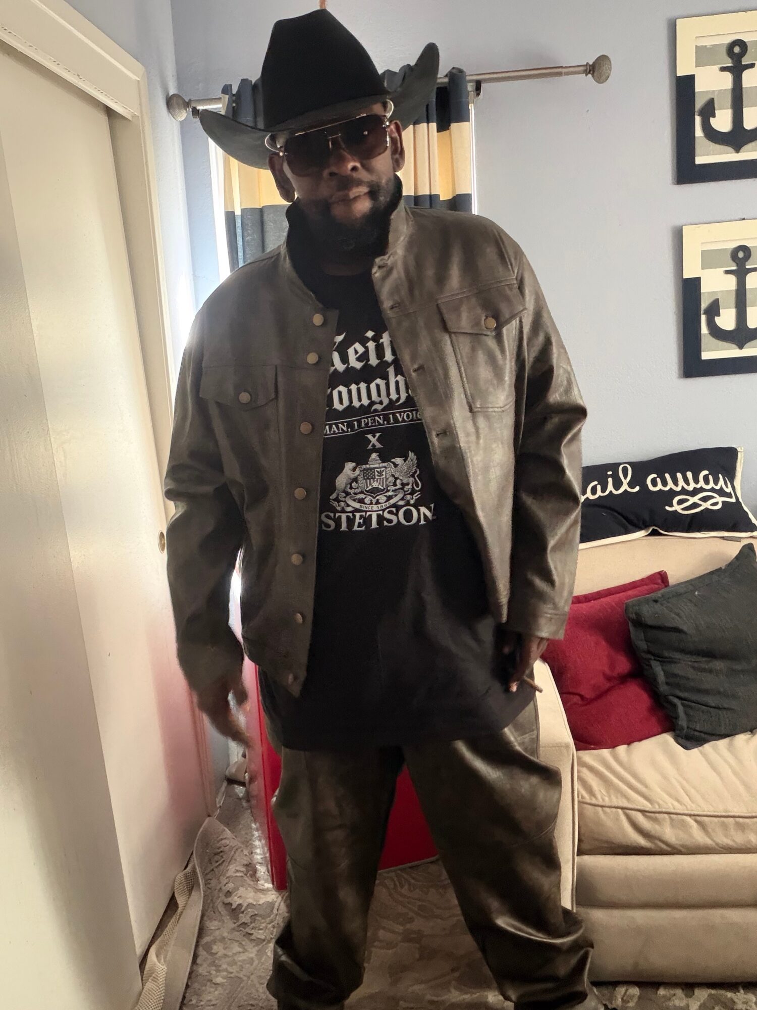 Man wearing a hat, sunglasses, and casual clothing standing in a room with nautical decor.