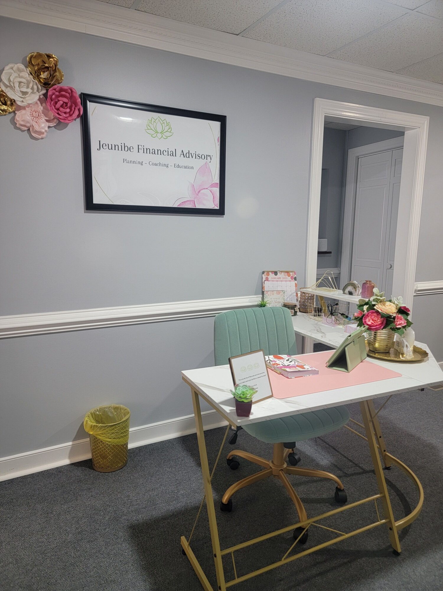 A white table with a pink folder, a green box, a small plant, and a gold candle holder, with a gold cart nearby.
