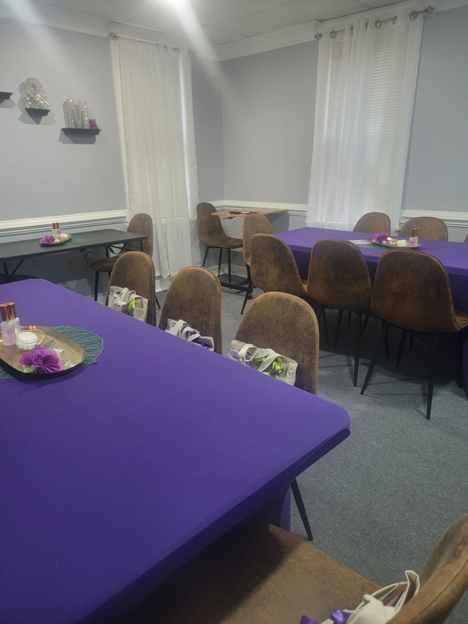 Room with purple tablecloths, chairs, and a table with a decorative plate, set in a room with white curtains and a window.