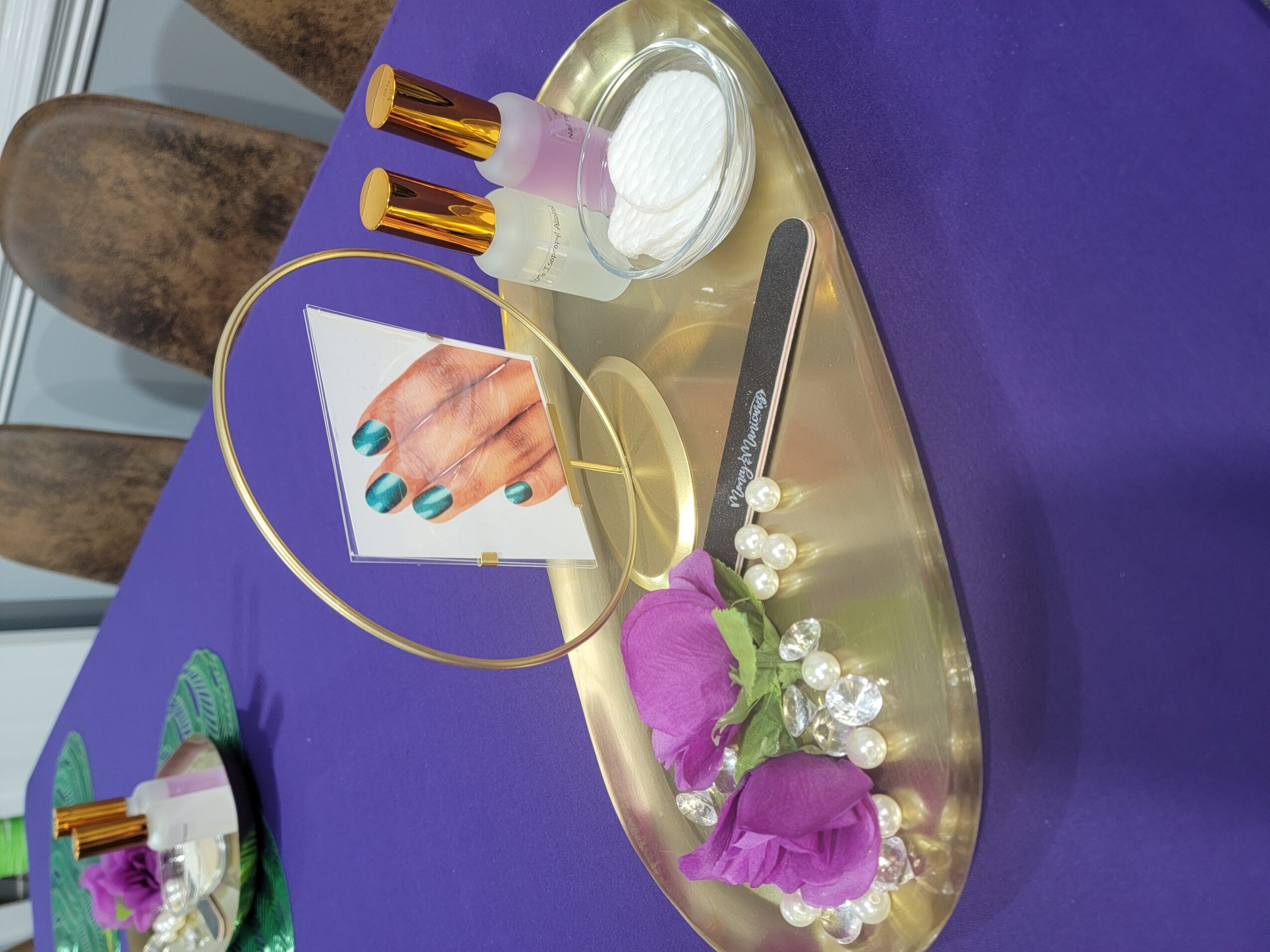 Decorative tray with nail polish bottles, a photo of painted nails, and flowers on a purple table.