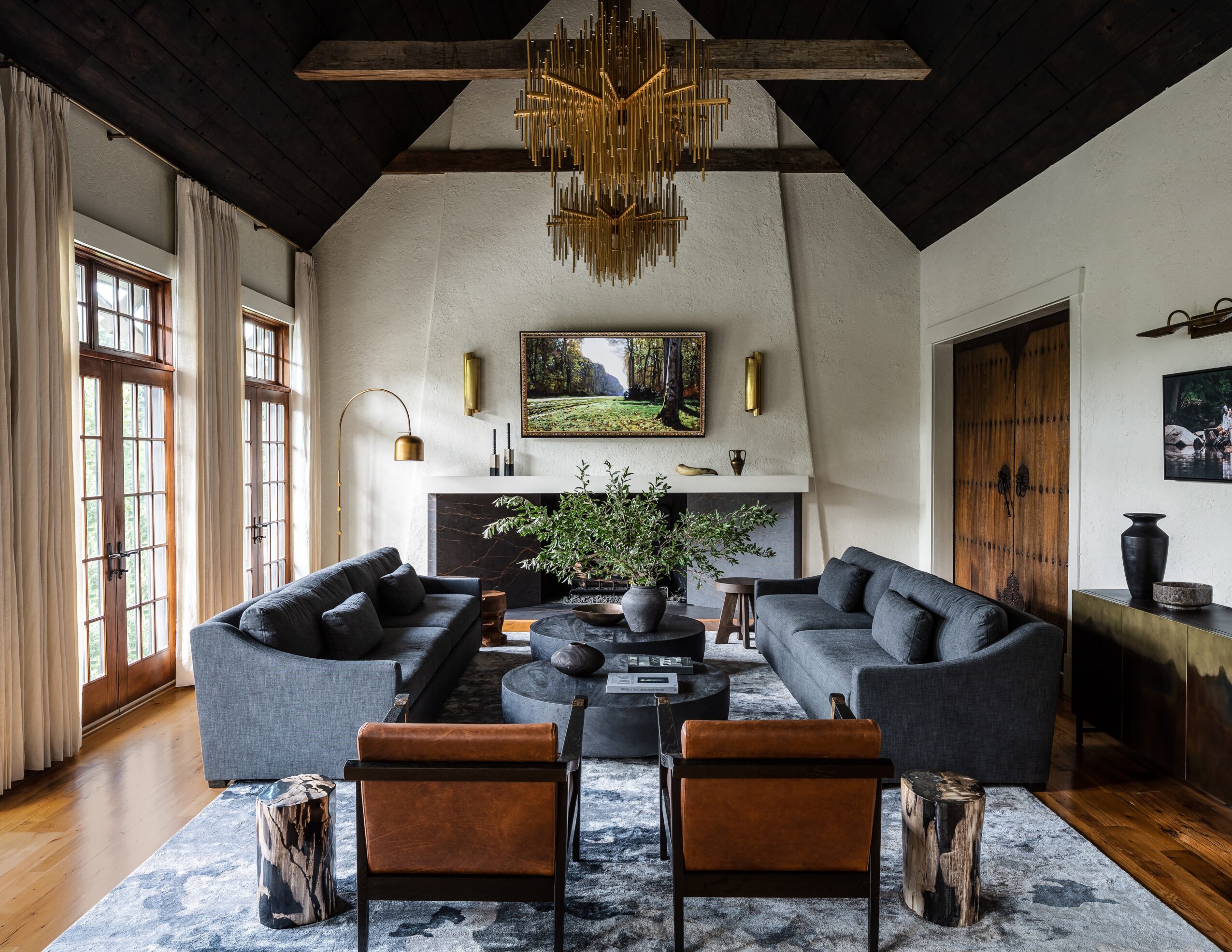 Living room with two dark sofas, two brown chairs, a large painting, and a chandelier, with large windows and a fireplace.