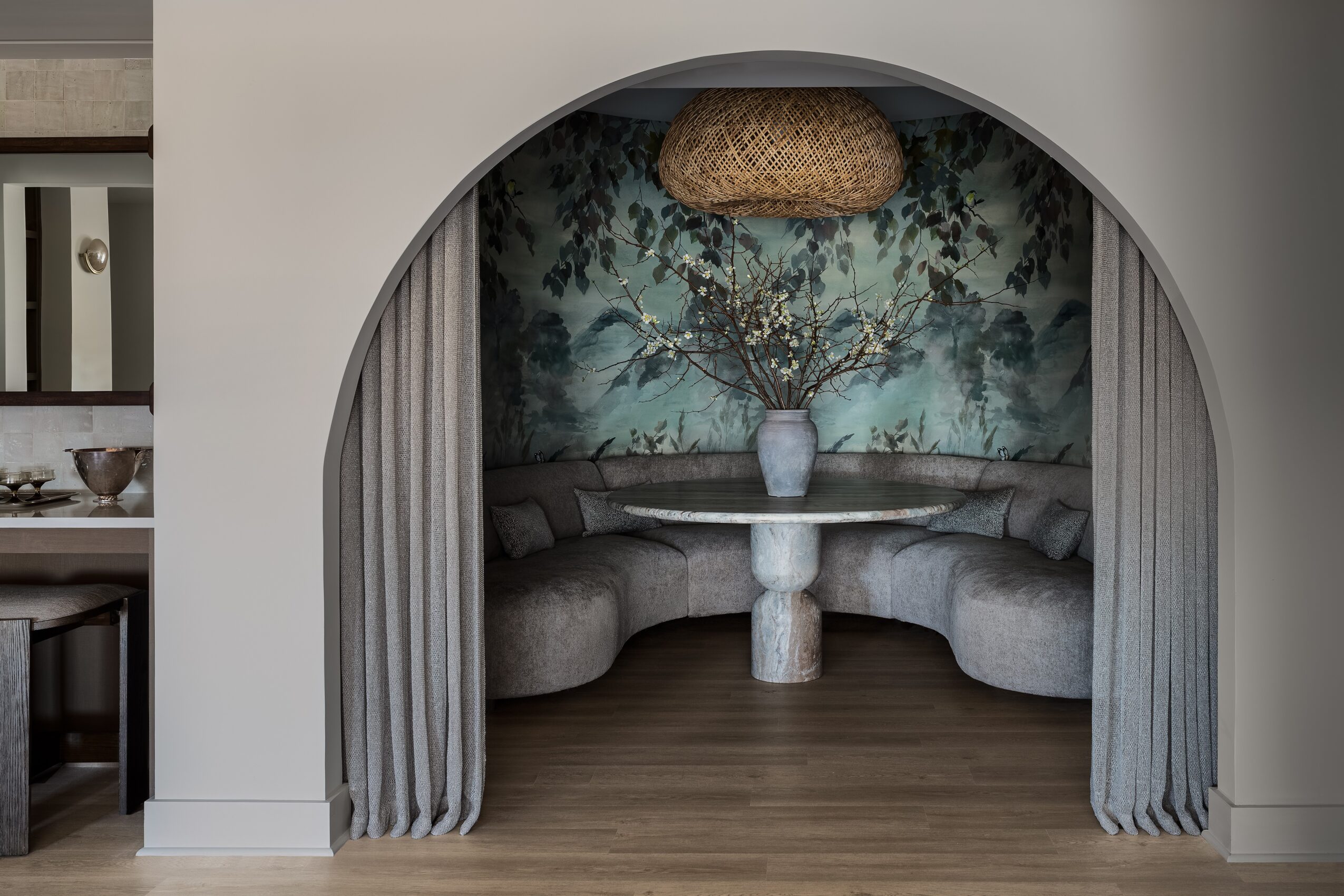Cozy nook with curved seating, a floral mural, a hanging light, and curtains on each side.