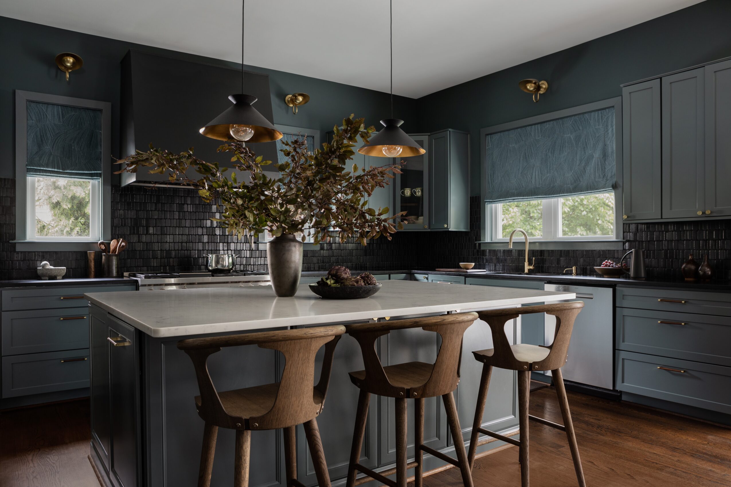 Kitchen with a central island, three chairs, gray cabinets, windows, and a vase with flowers on the island.