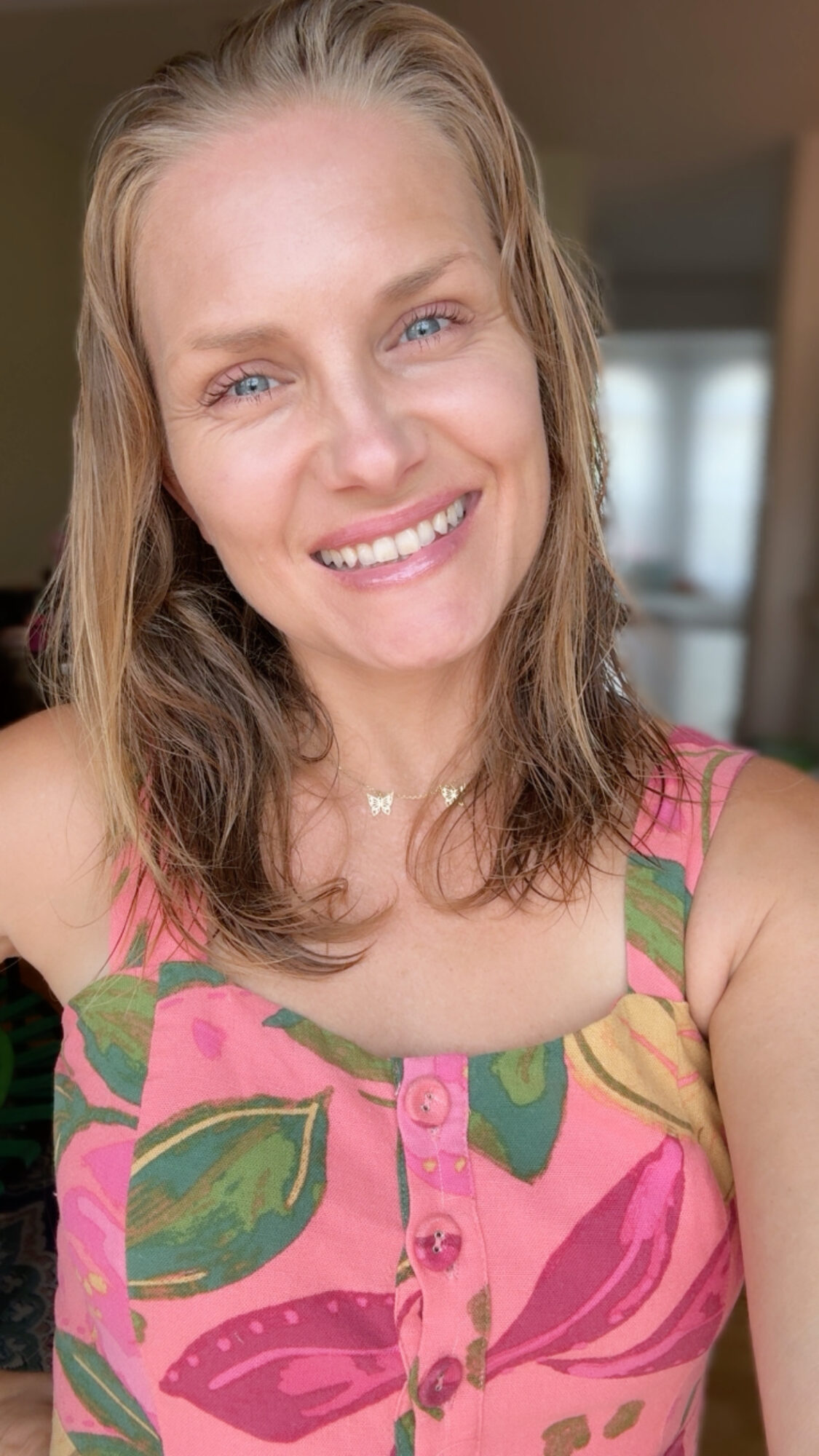 Smiling woman with shoulder-length hair wearing a colorful patterned top indoors.