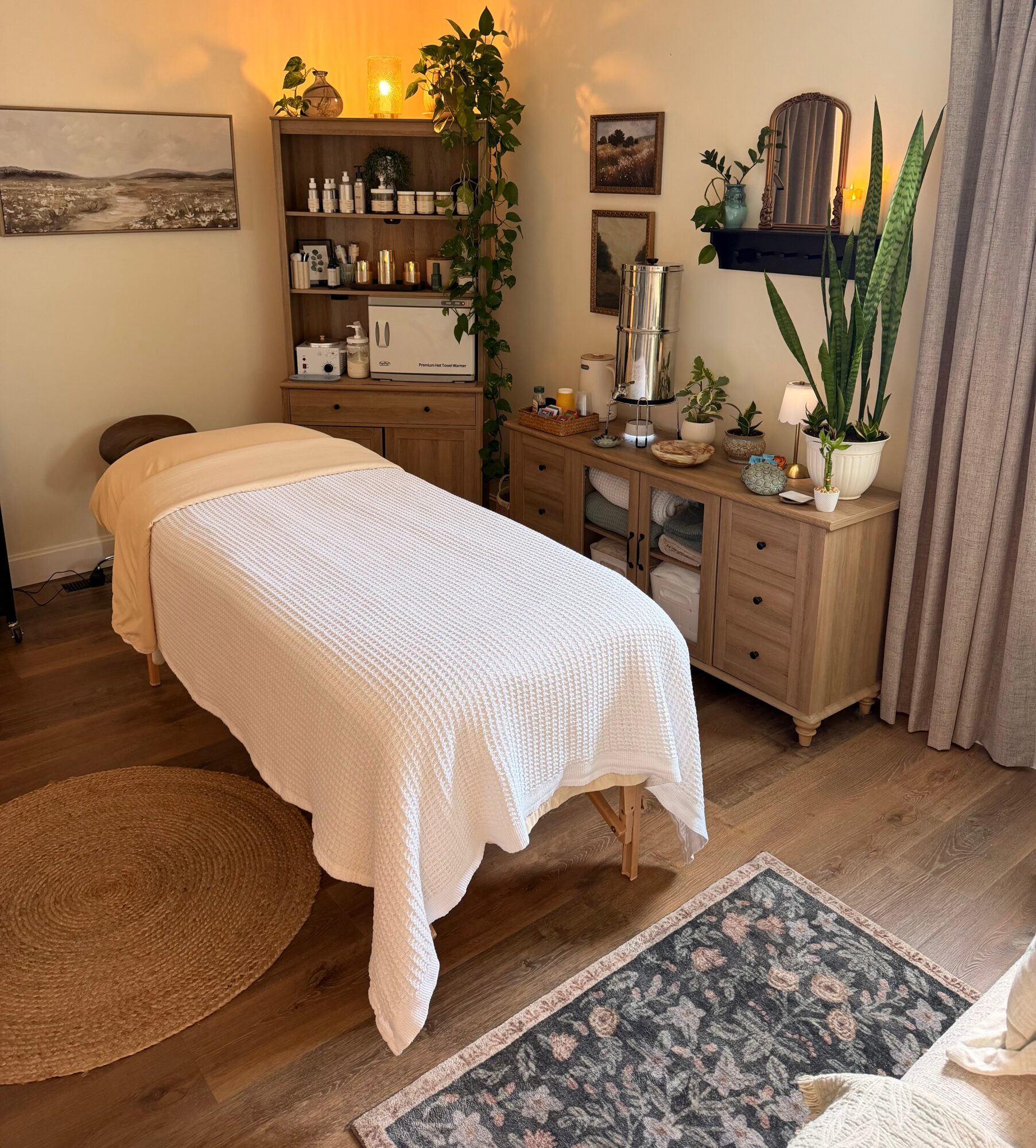 Massage table covered with white blanket in a cozy room with wooden furniture, plants, and decorative items.