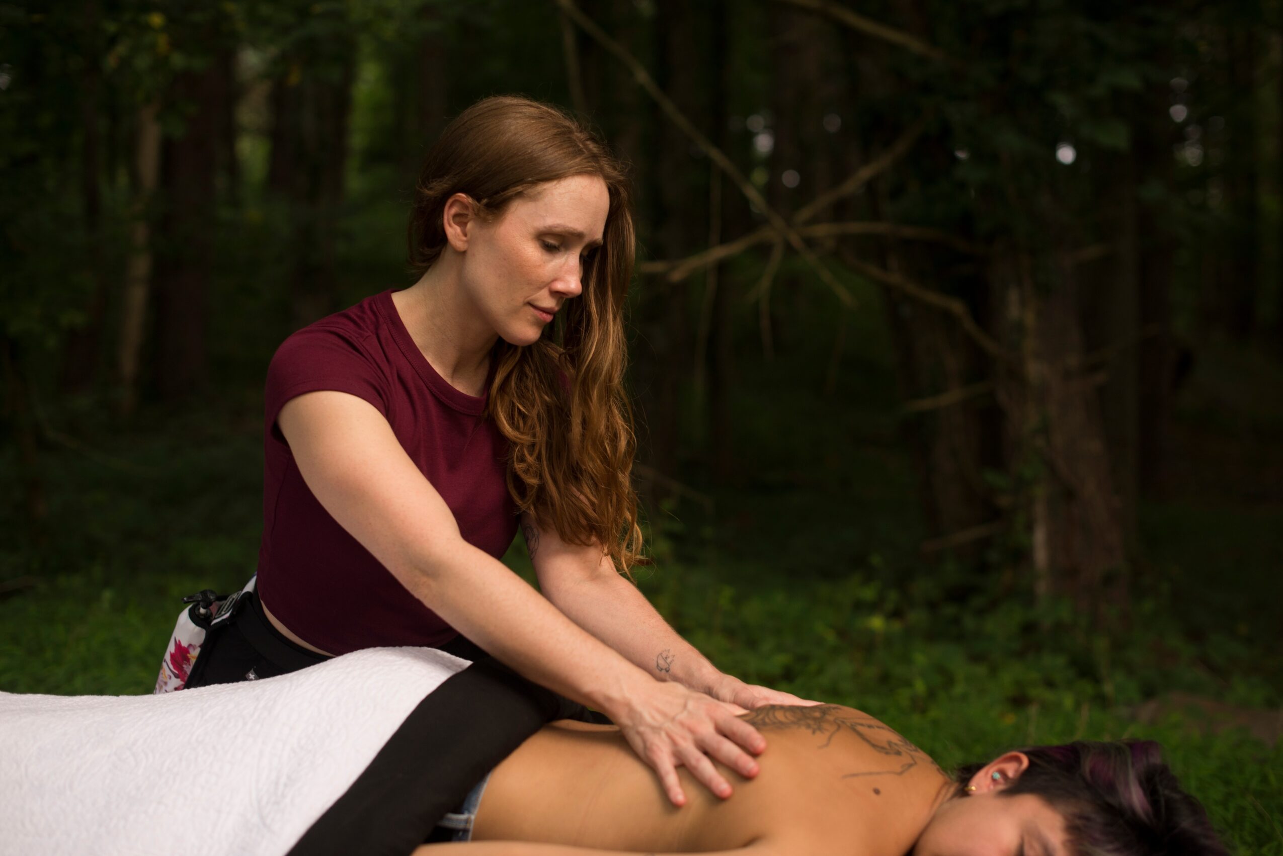 Woman with long hair touching a person's leg outdoors in a forest setting.