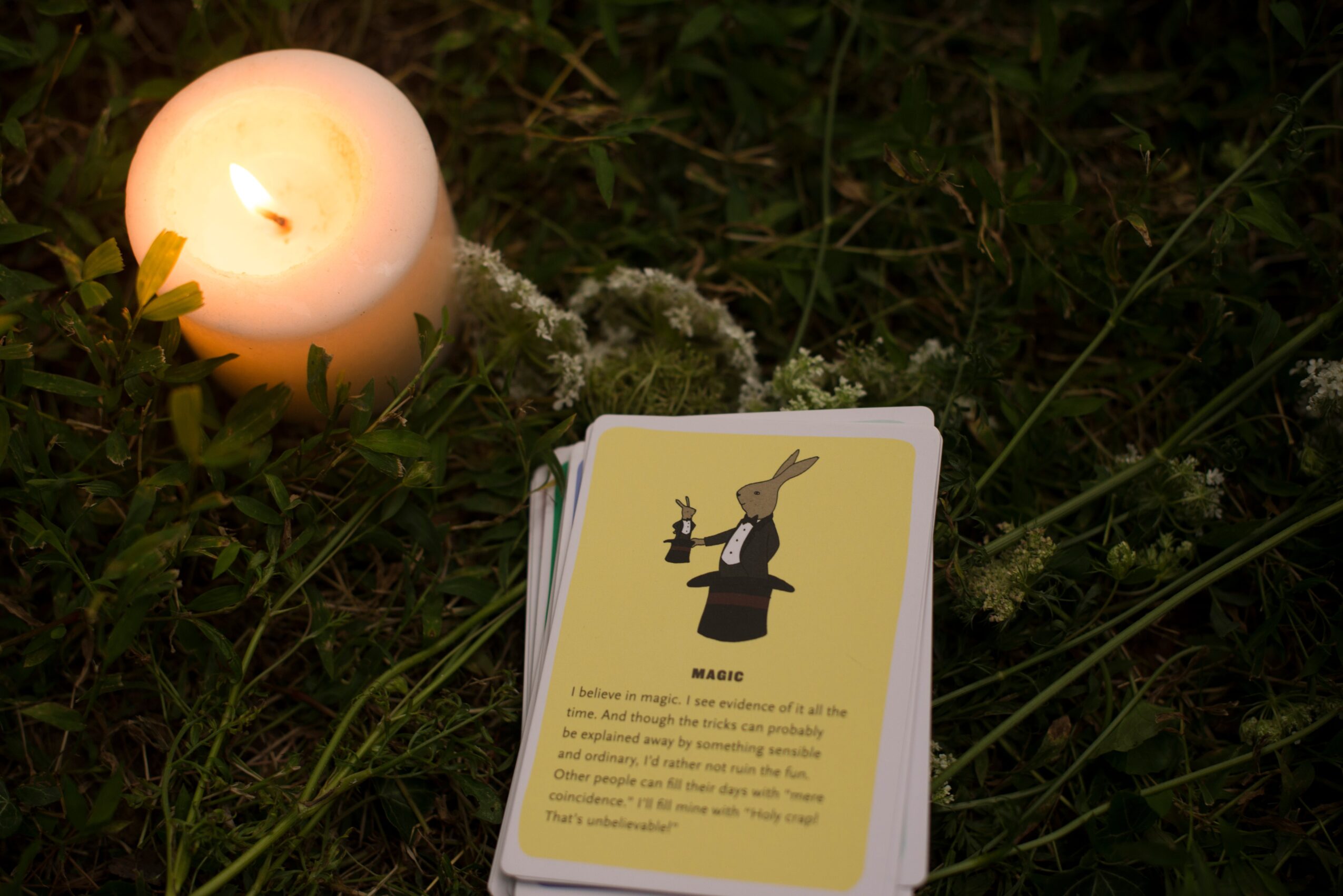 A lit candle and a card with a witch illustration on grass at night.