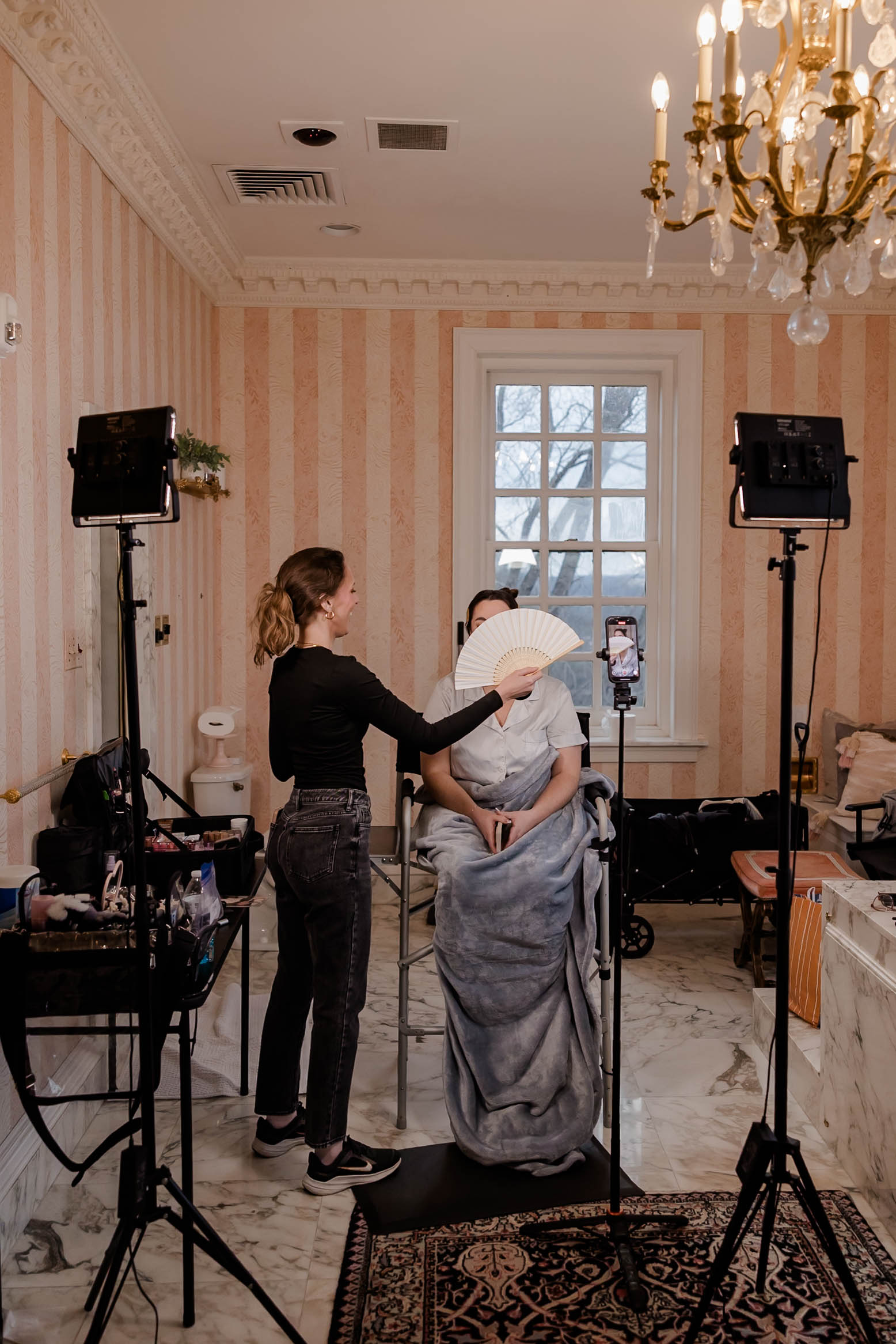 Person receiving a makeup or skincare treatment in a decorated room with a chandelier, window, and audio equipment.