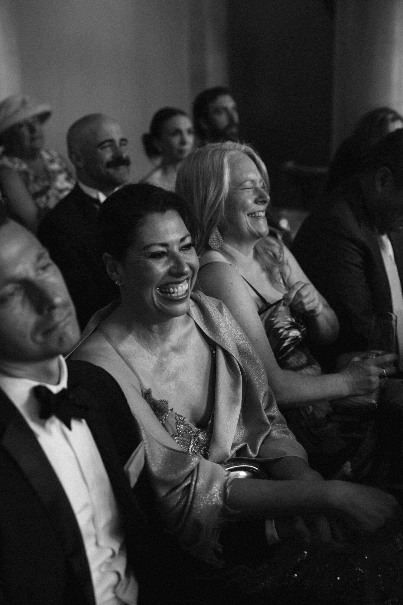 Group of people seated, smiling and laughing, at a formal event, in black and white.