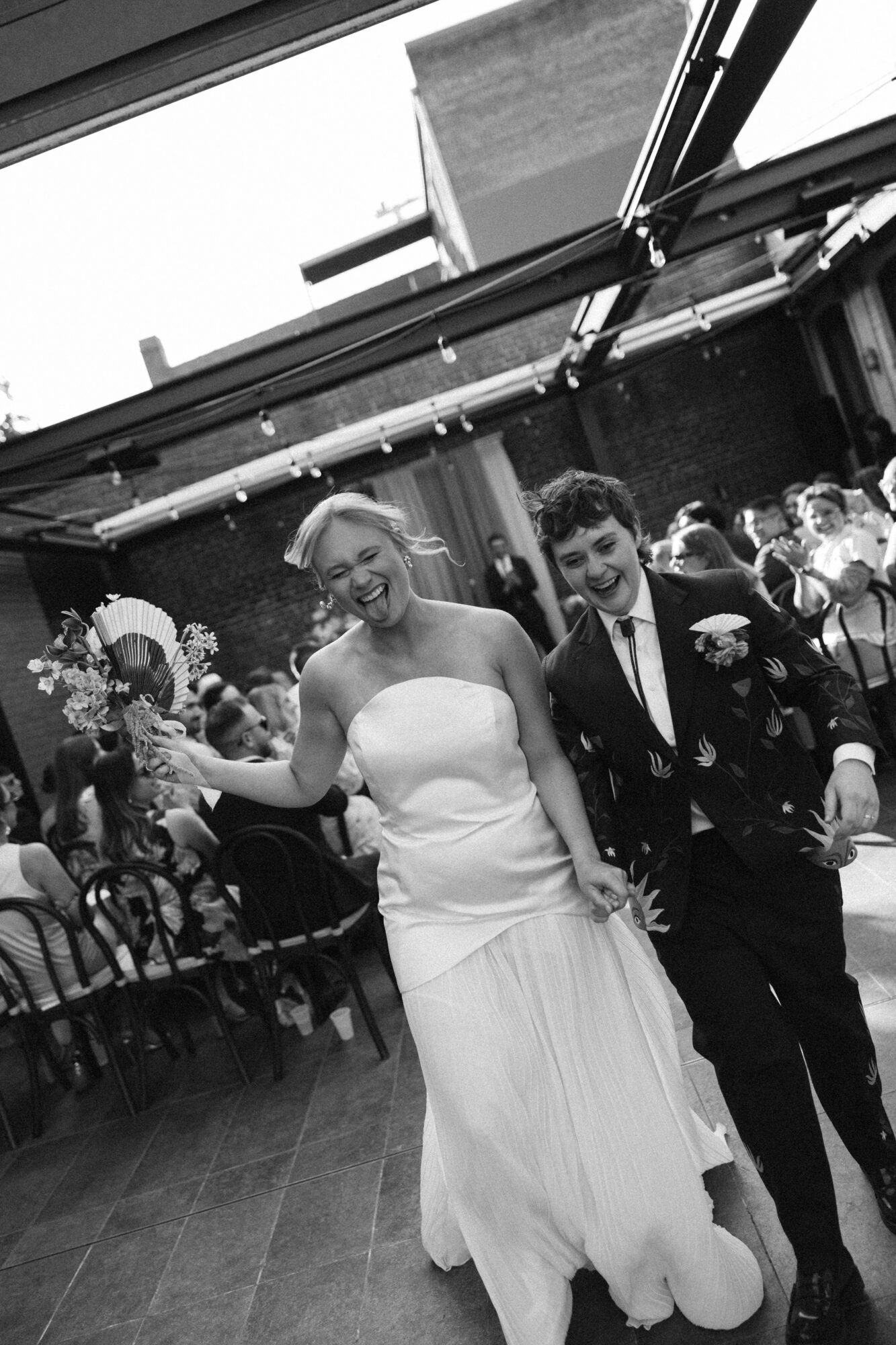 Bride and groom smiling and dancing at wedding reception, surrounded by guests, in a decorated venue.