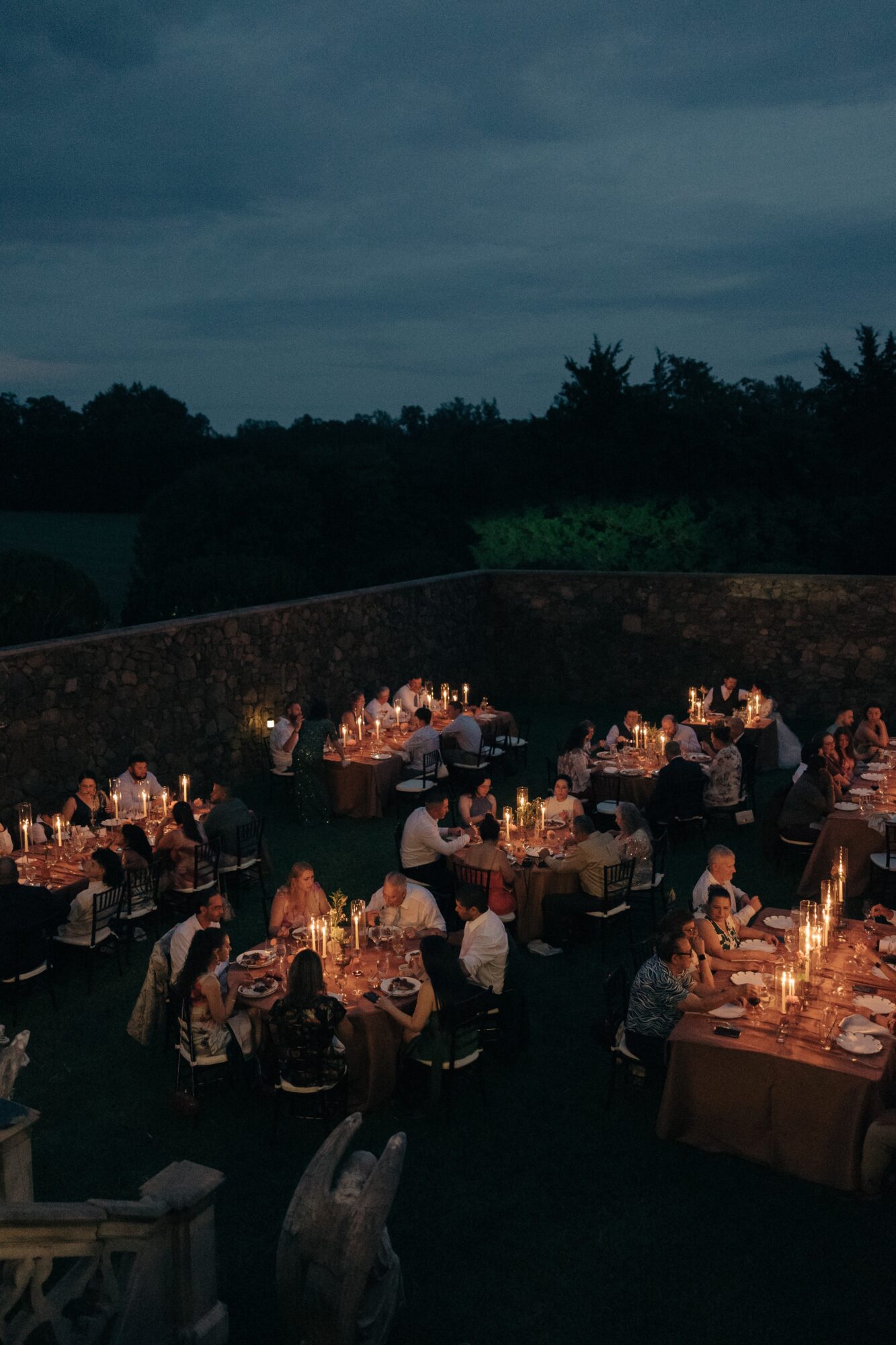 Outdoor evening event with tables, candles, and people dining under a dark sky.