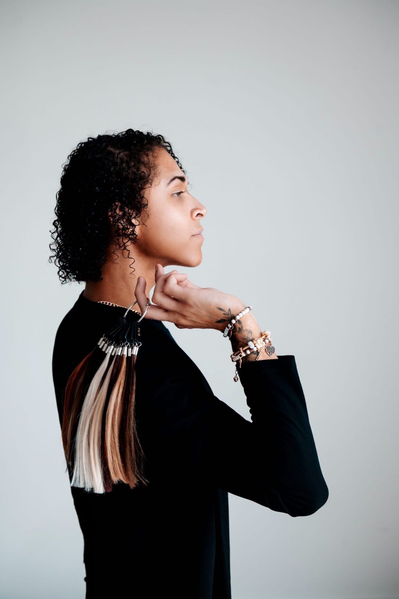 Profile of a woman with curly hair, wearing a black top, looking to the right, with her hand near her neck.