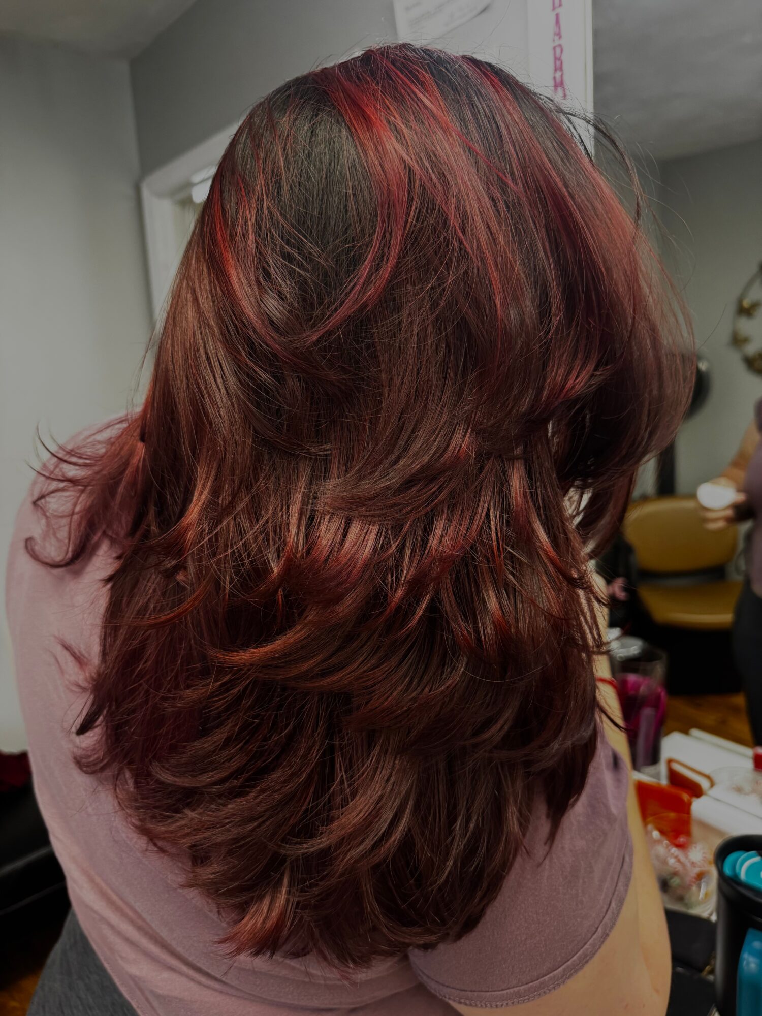 Back view of a person with long, wavy hair dyed in shades of red and brown, indoors.