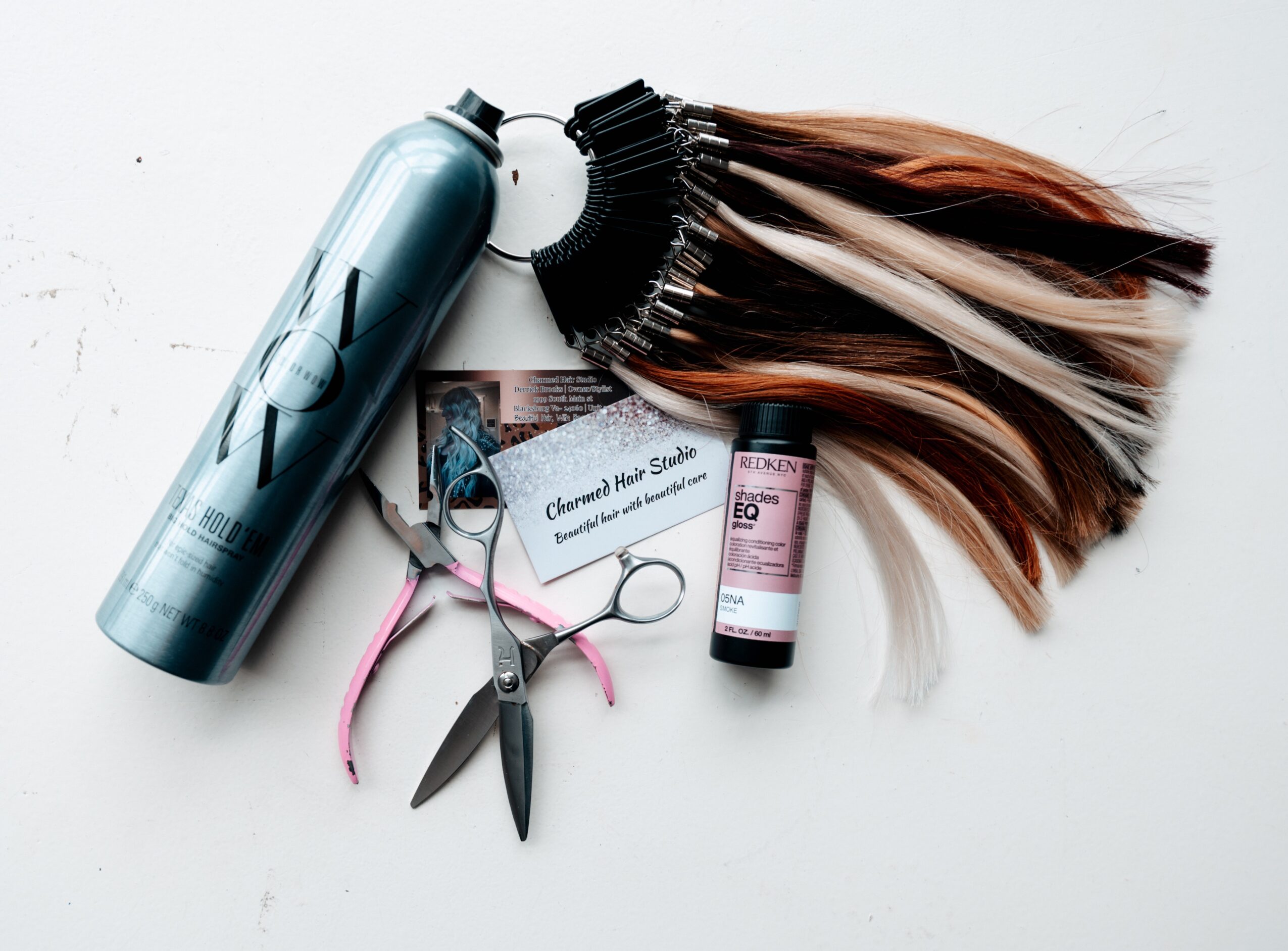Hair color swatches, scissors, a spray bottle, a small container, and a hairbrush with hair extensions on a white surface.