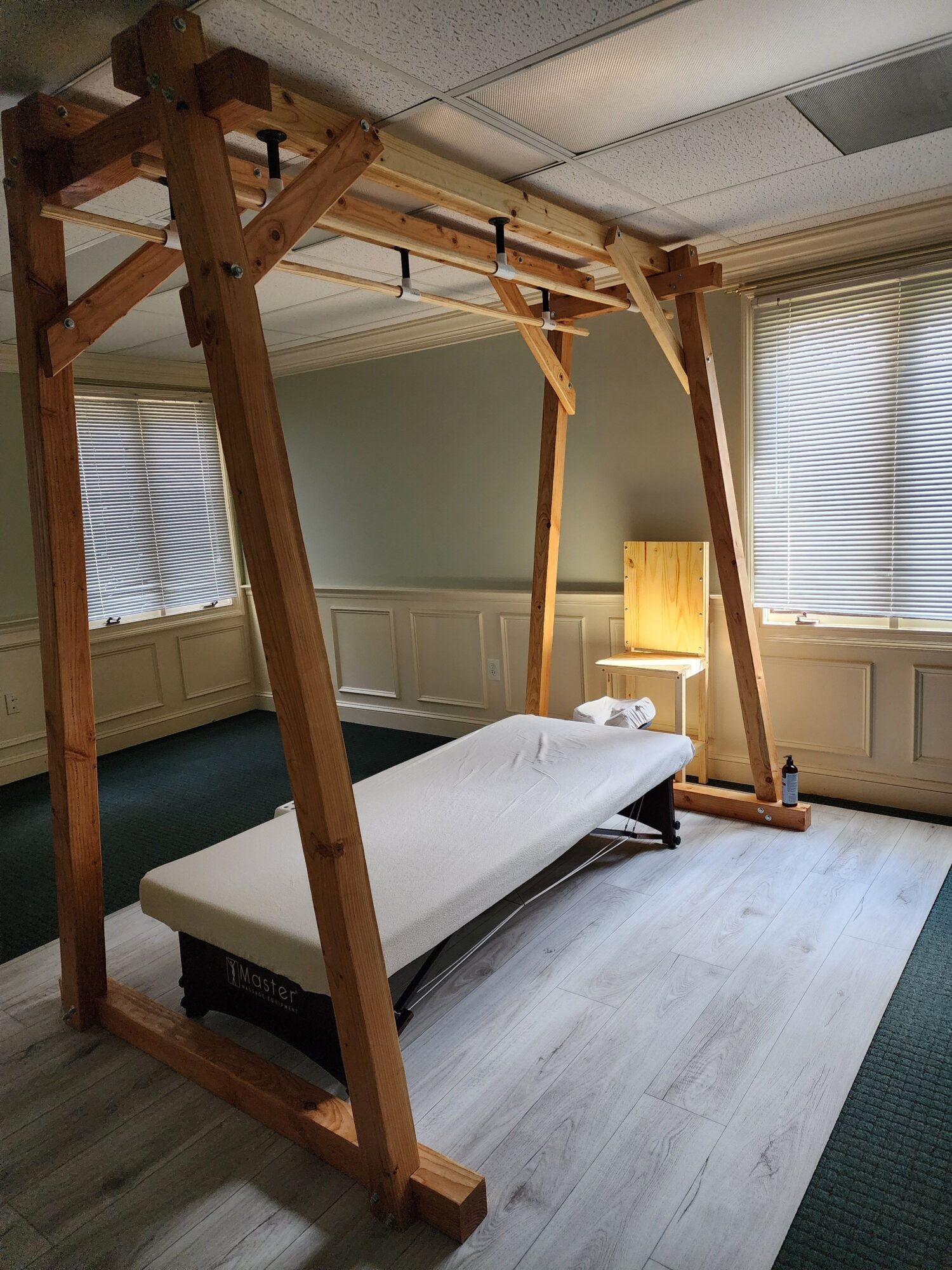 Wooden four-poster bed with white bedding in a room with green walls and windows, a yellow lamp, and a white ceiling.