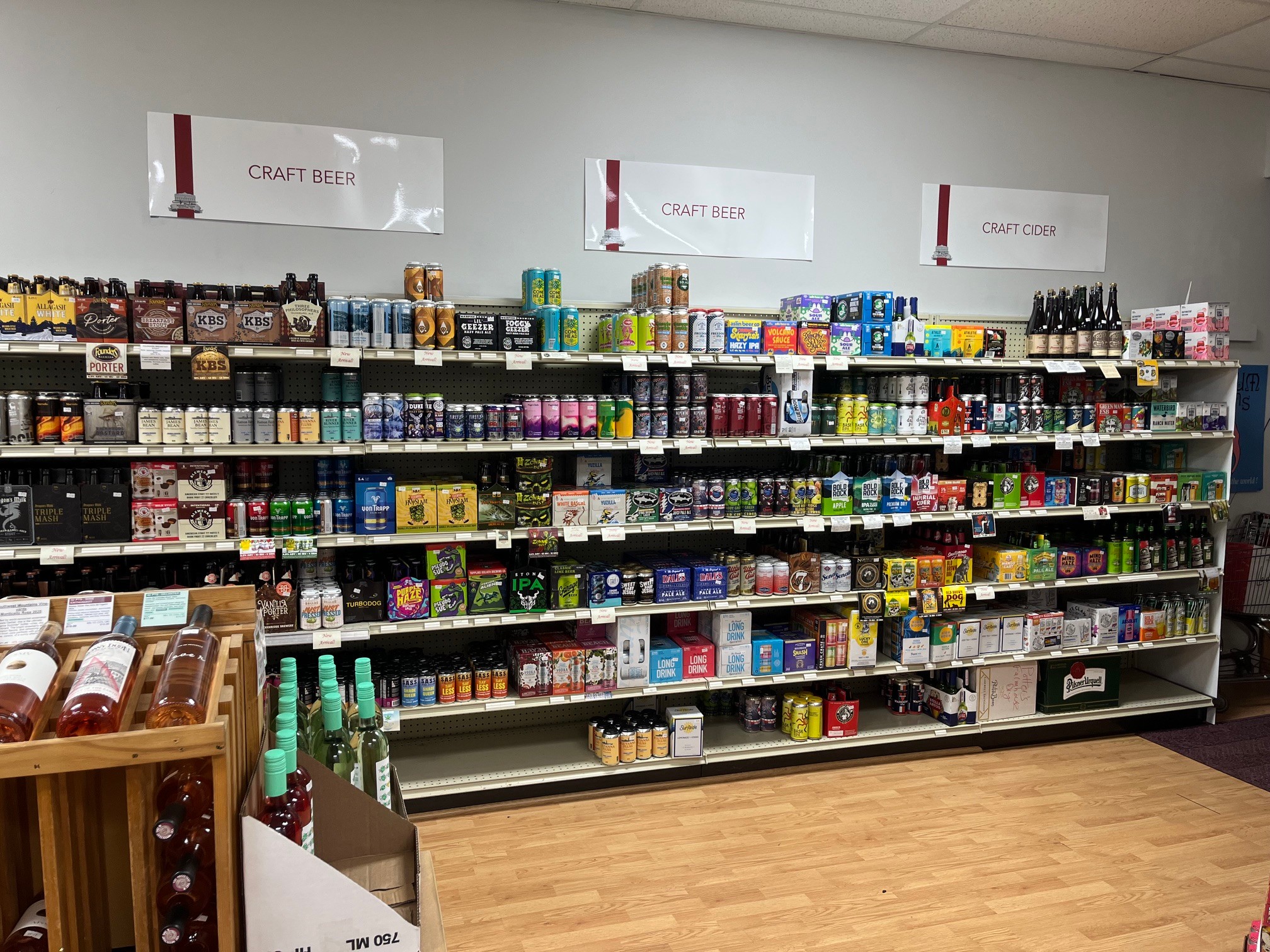 Shelves stocked with various canned and bottled beverages in a store aisle, with a wooden display on the left.