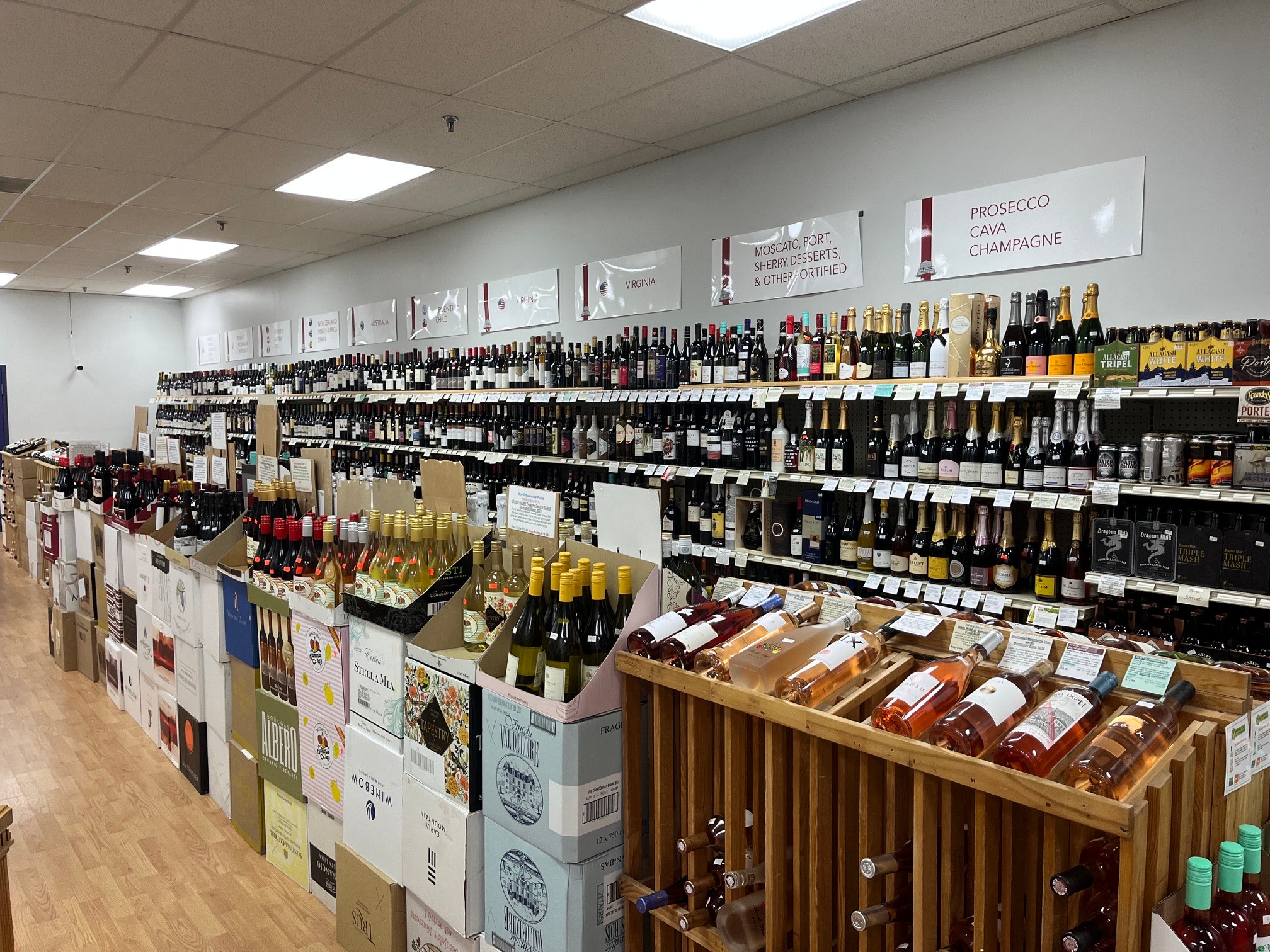 Store aisle with shelves stocked with bottles of wine and other beverages, and boxes of wine on the floor.