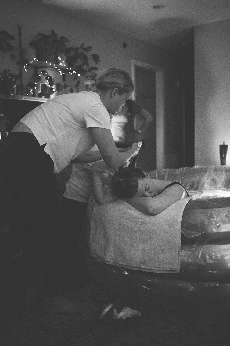 Person leaning over a child lying on a couch, with a decorated background and a dark room.