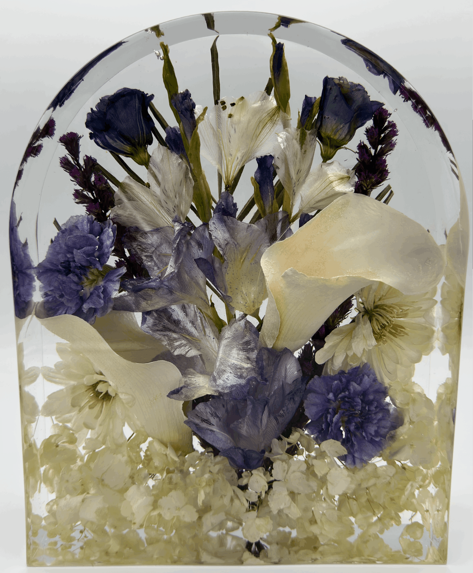 Pressed flowers including purple, white, and cream-colored blooms inside a glass dome.