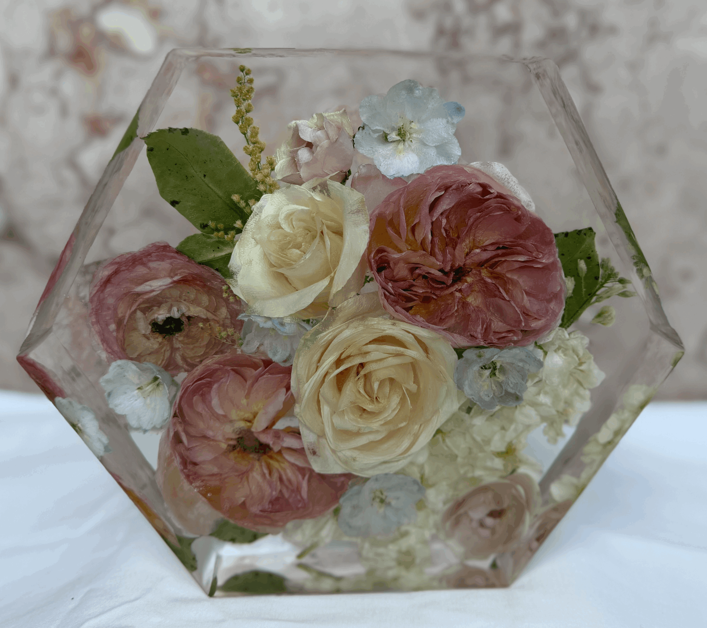 Flower arrangement with roses and other flowers in a glass container, viewed from the side.