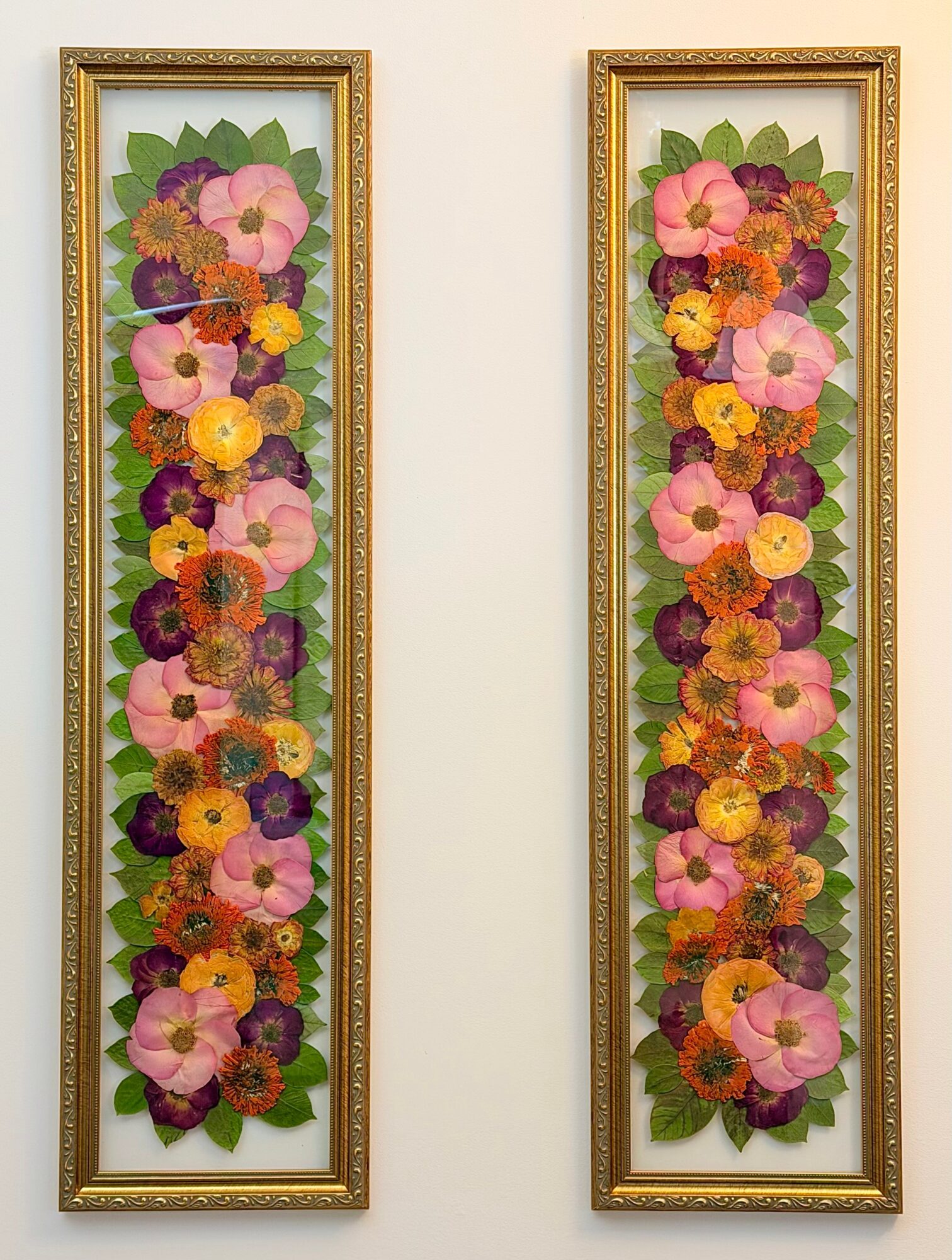 Two vertical floral artwork frames with colorful flowers and green leaves, hung side by side on a white wall.