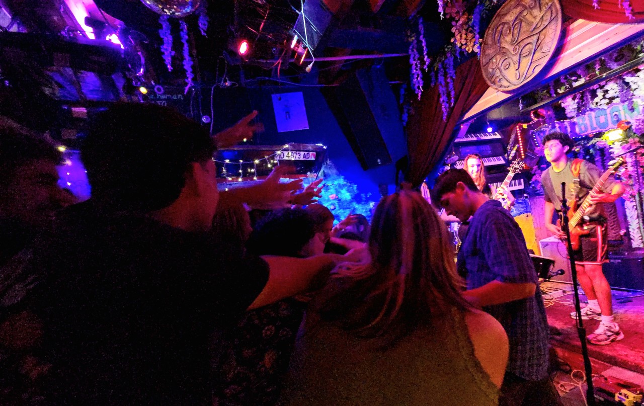 People dancing and enjoying live music in a dimly lit bar or club with colorful lighting.