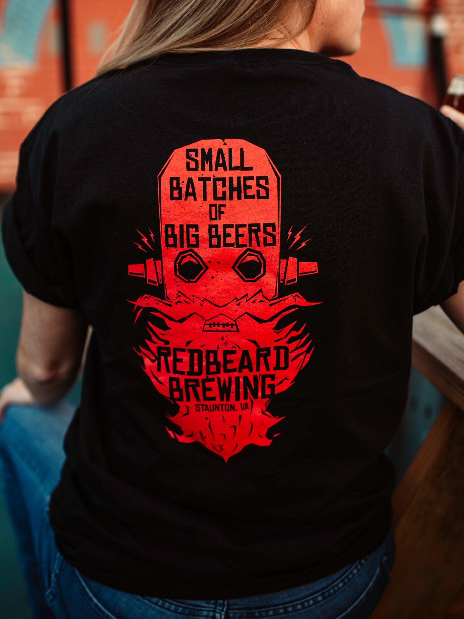 Back of a person wearing a black T-shirt with red skull and text design for Redbeard Brewing.