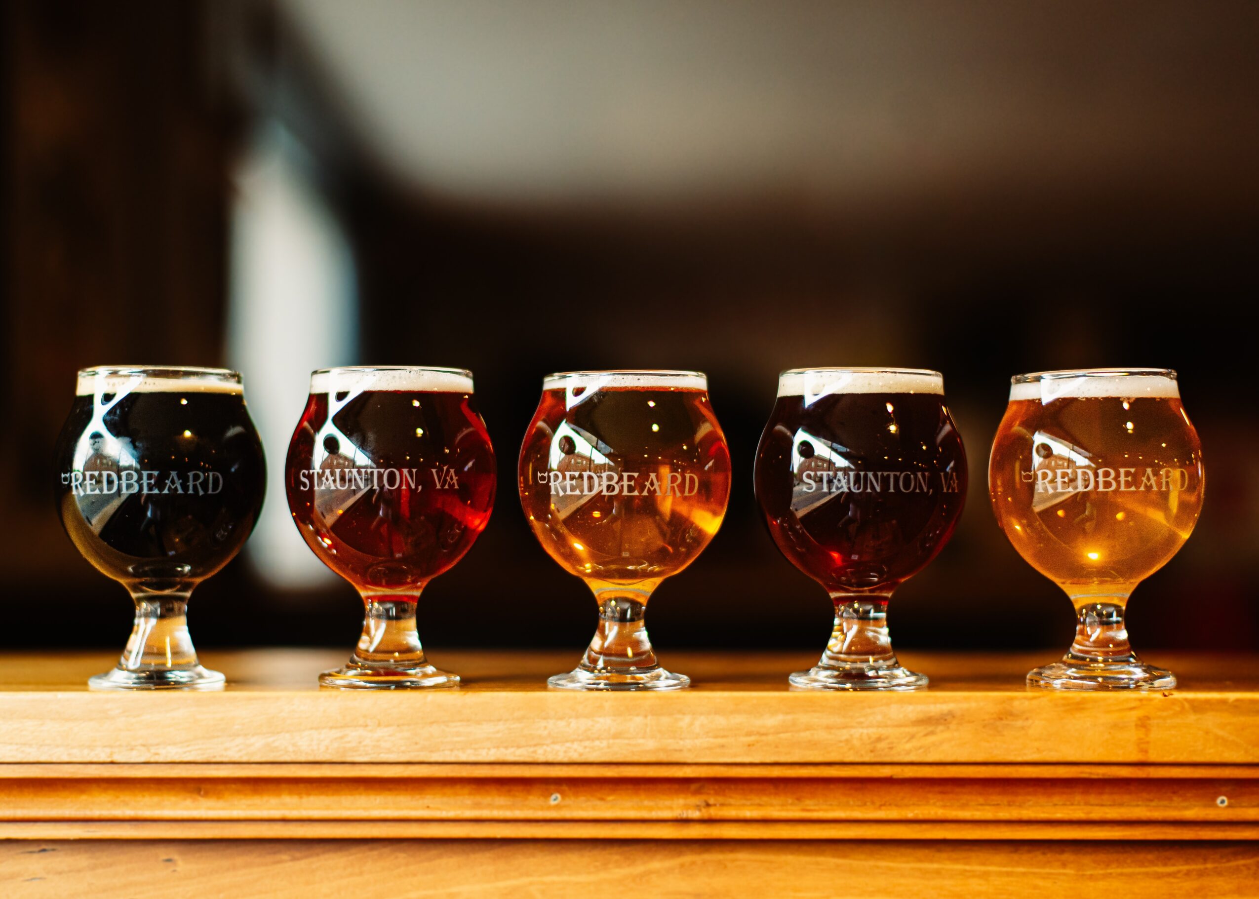 Five glasses of beer on a wooden surface with a blurred background.