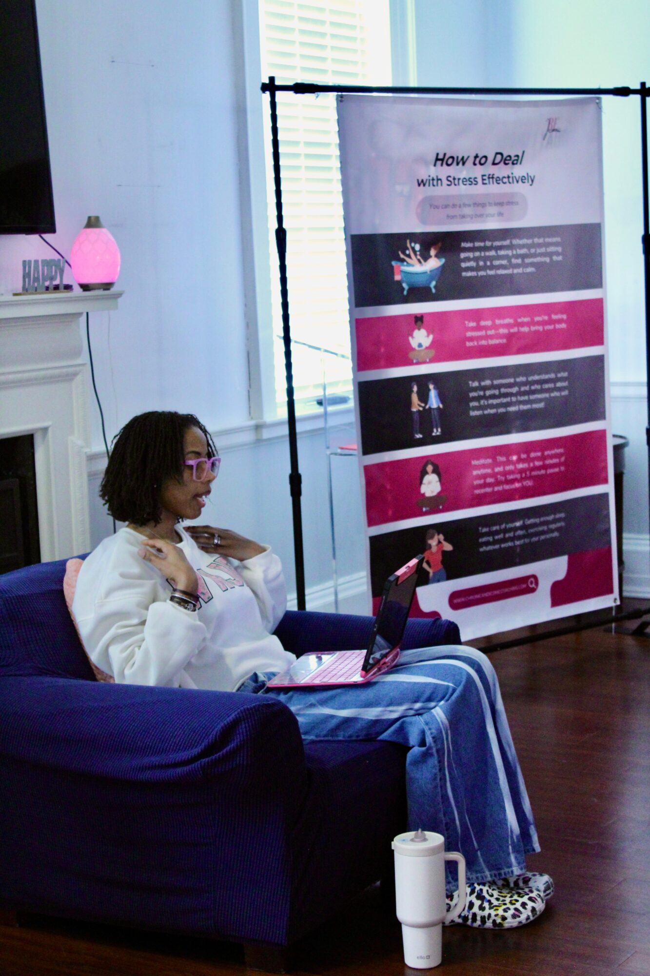 Woman sitting on a blue couch, pointing at a vertical banner with health tips, in a room with a window and a white fireplace.