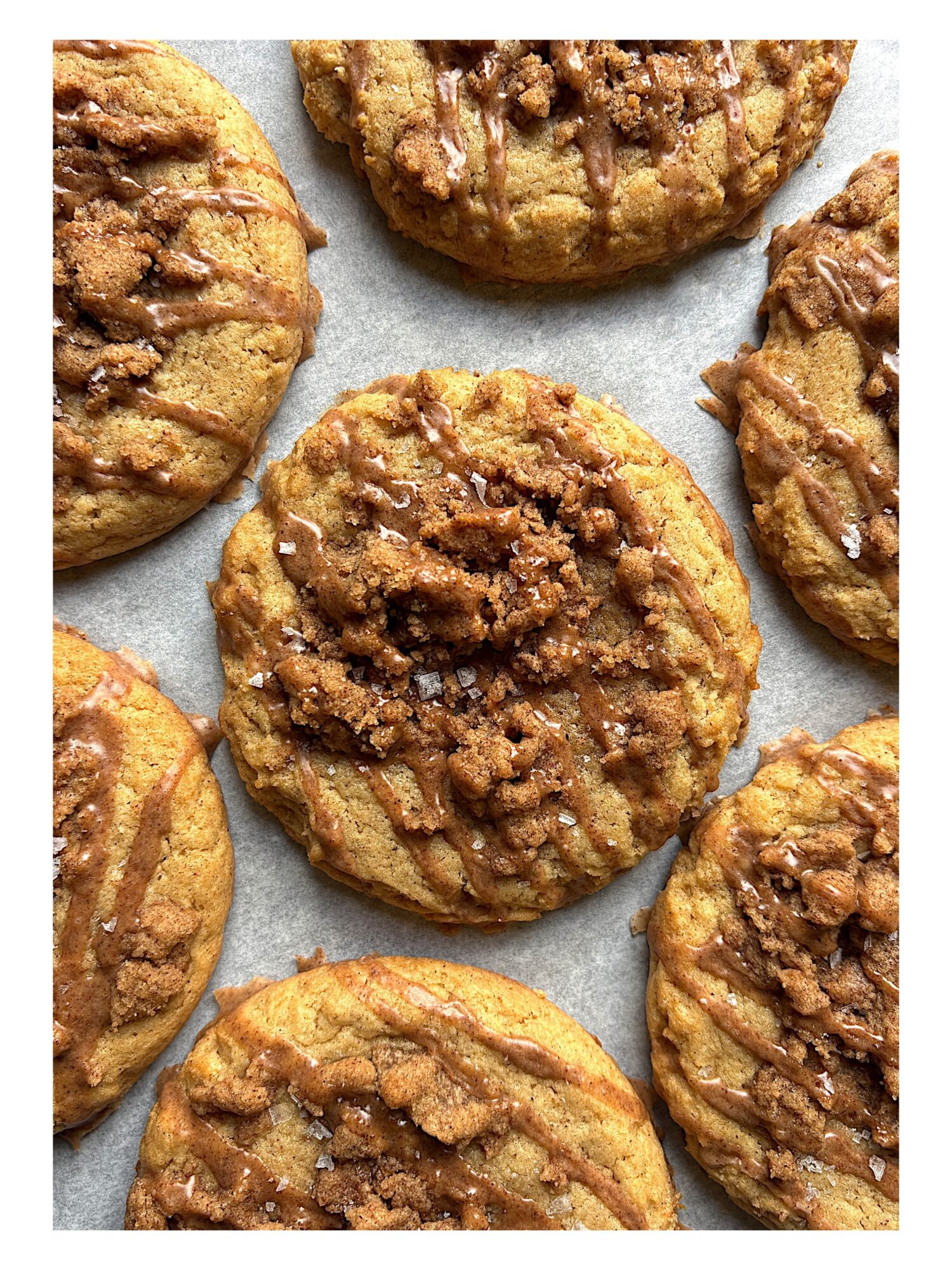 Close-up of several cookies with a crumbly topping on a parchment paper-lined surface.