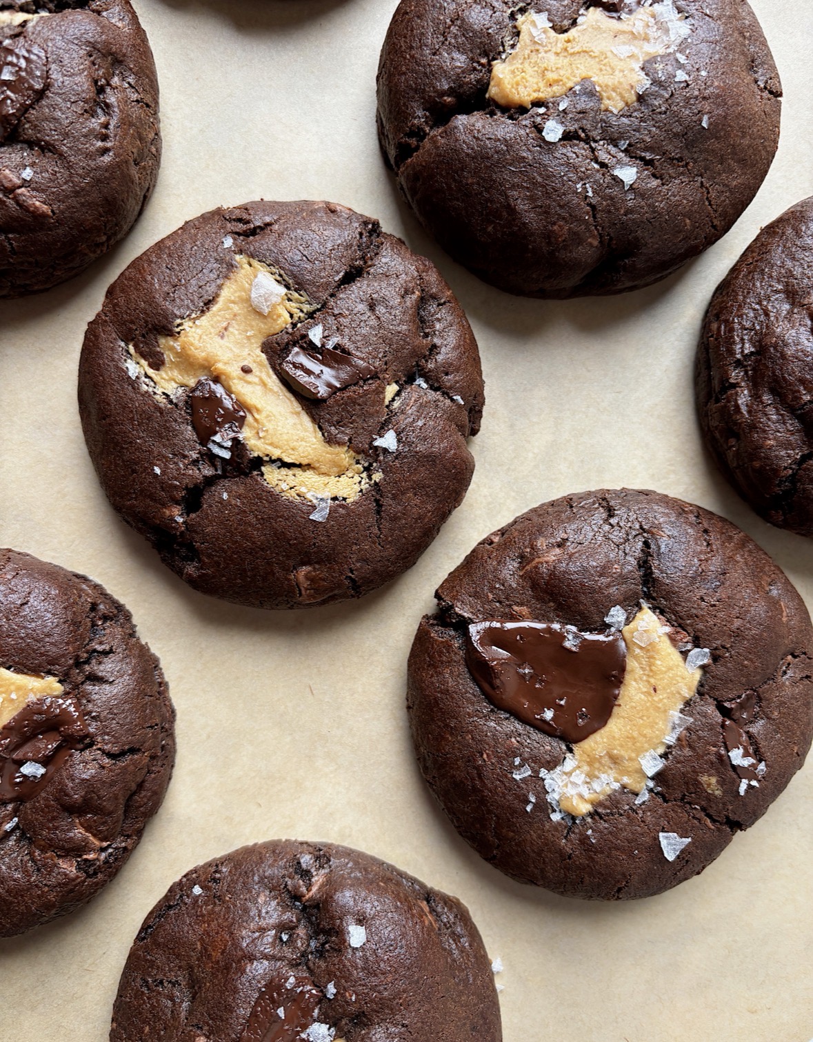 Chocolate cookies with chunks of chocolate and a light-colored filling, on parchment paper, close-up view.