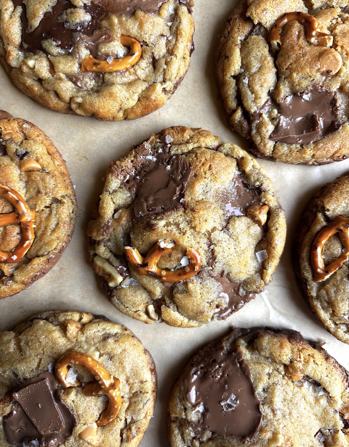 Close-up of chocolate chip cookies with pretzel pieces on parchment paper.