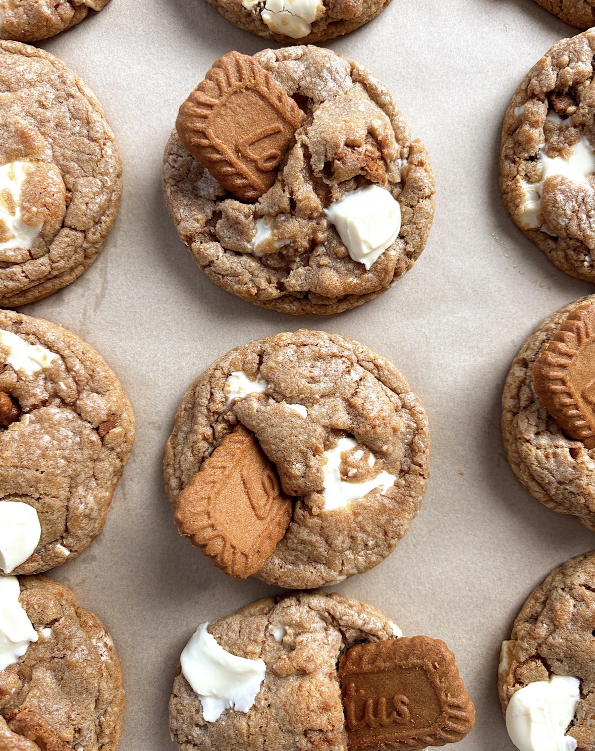 Close-up of cookies with chocolate, white chocolate, and biscuit pieces on a light surface.