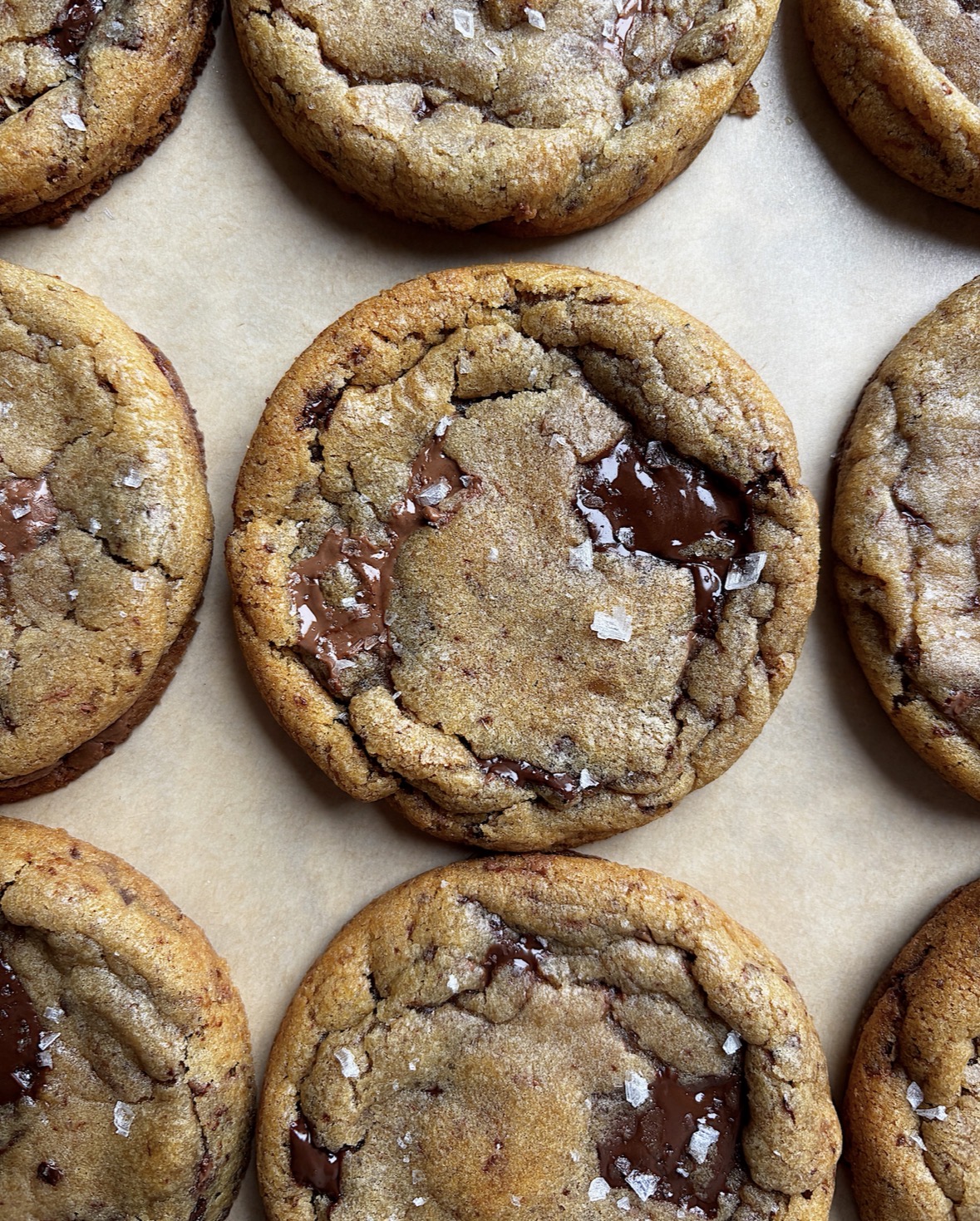 Close-up of chocolate chip cookies on parchment paper, showing golden-brown edges and melted chocolate chunks.