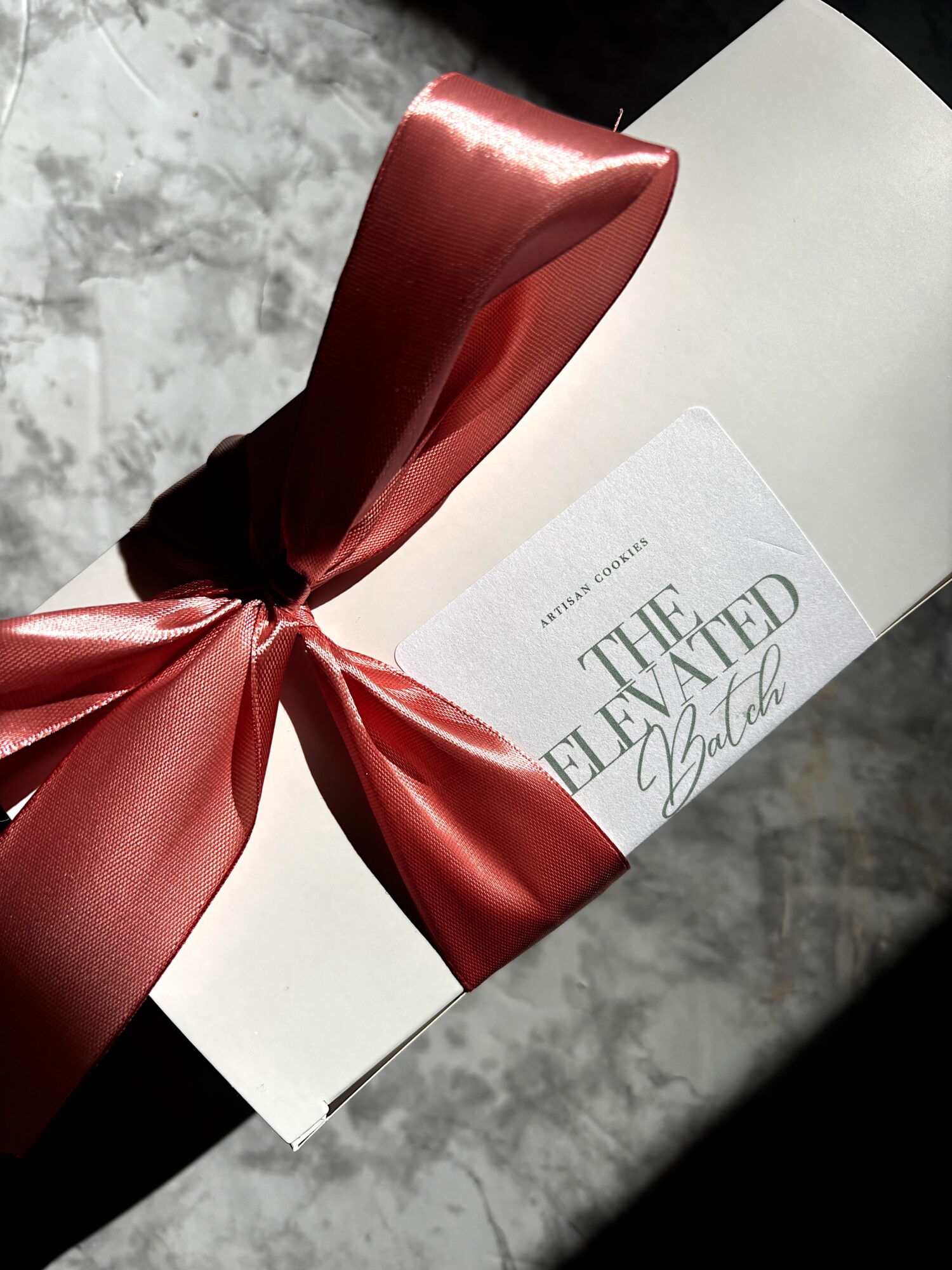 A white box with a red satin ribbon tied in a bow, partially covering a card with text.