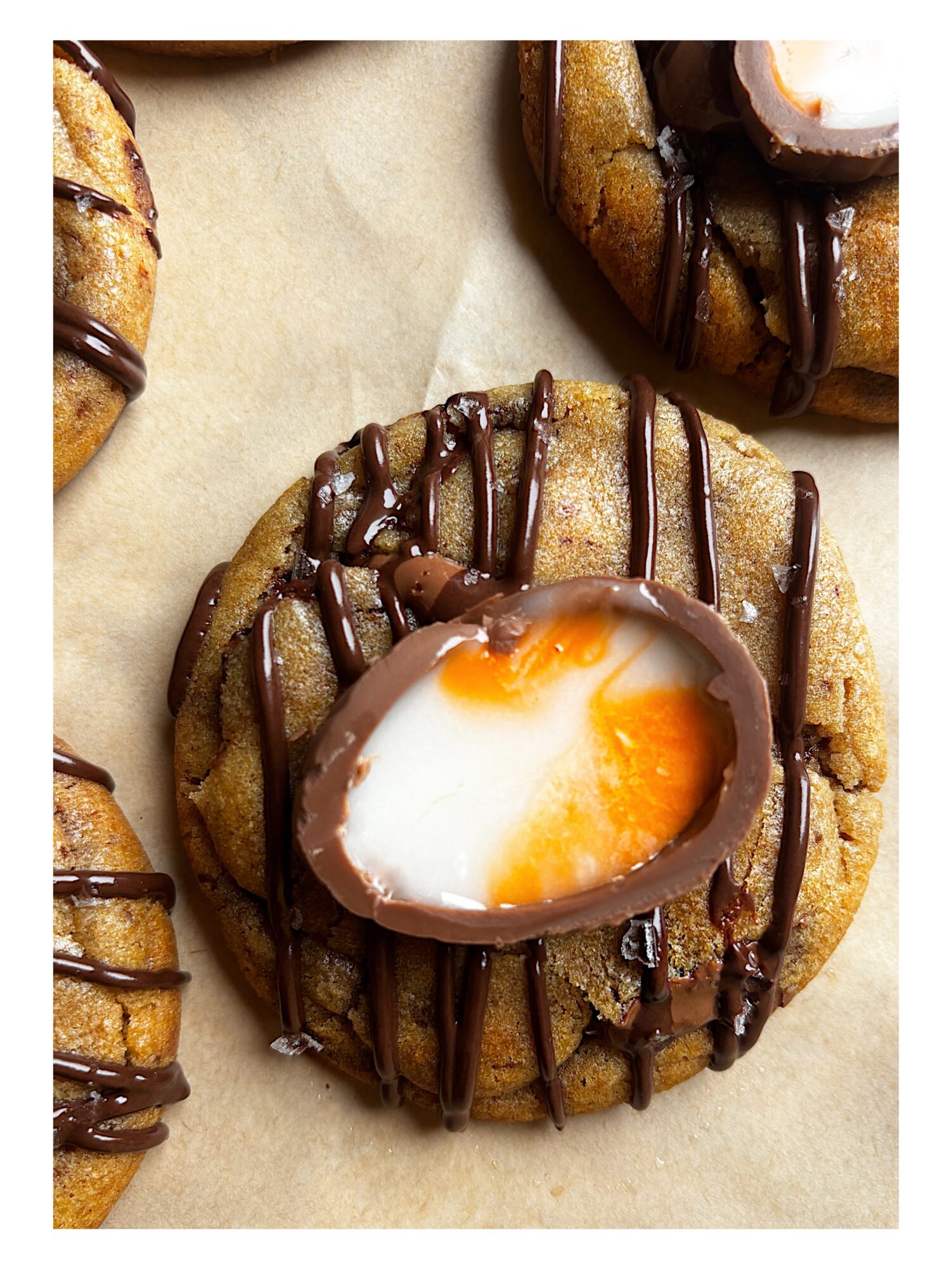 Cookie with a halved chocolate egg, drizzled with chocolate, on parchment paper.