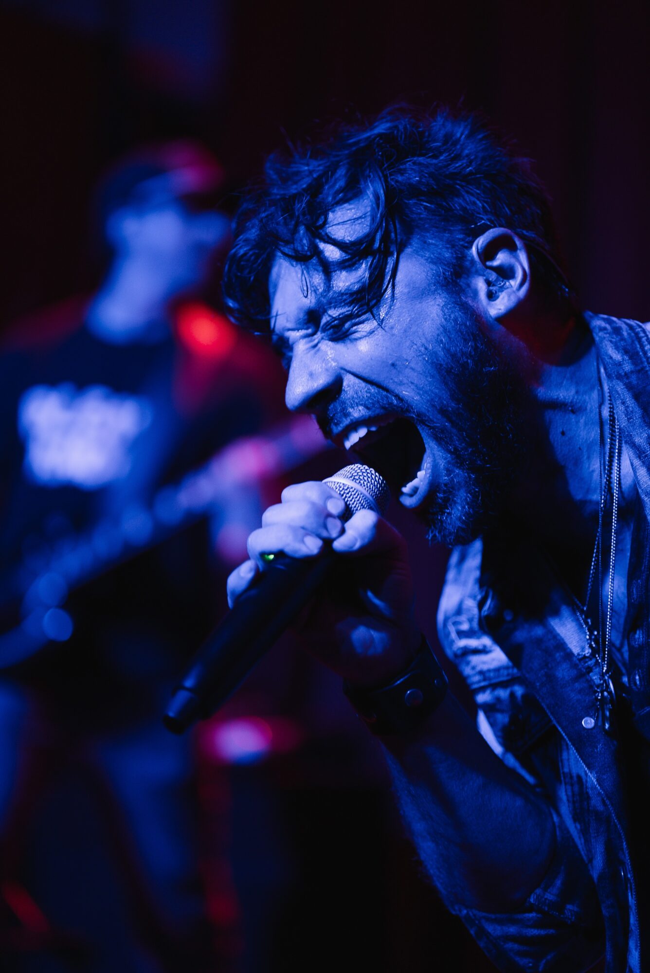Person passionately singing into a microphone with a blurred background, dark lighting, and blue tones.