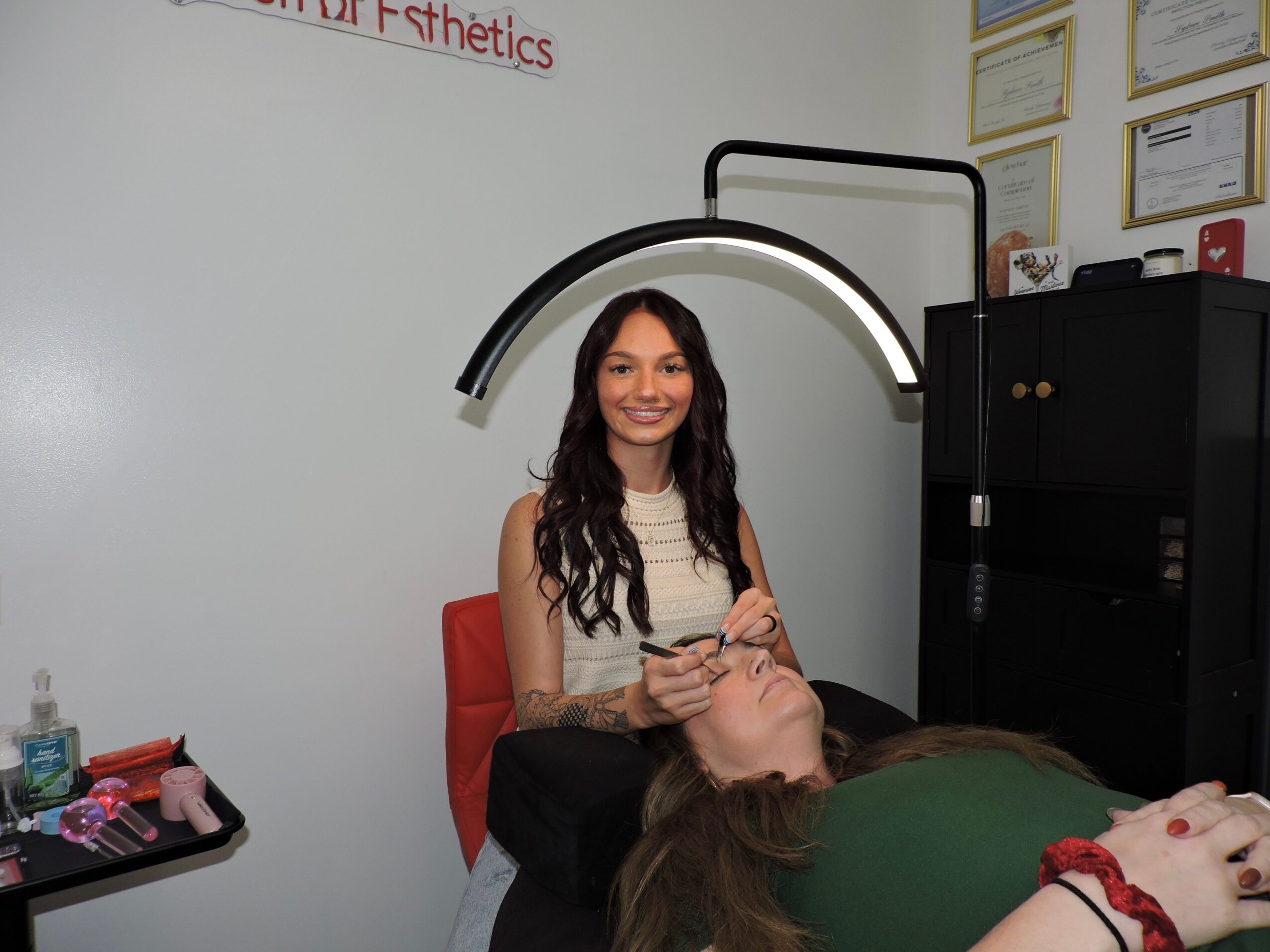 Woman with long dark hair sitting in a chair, smiling, in a room with certificates on the wall.