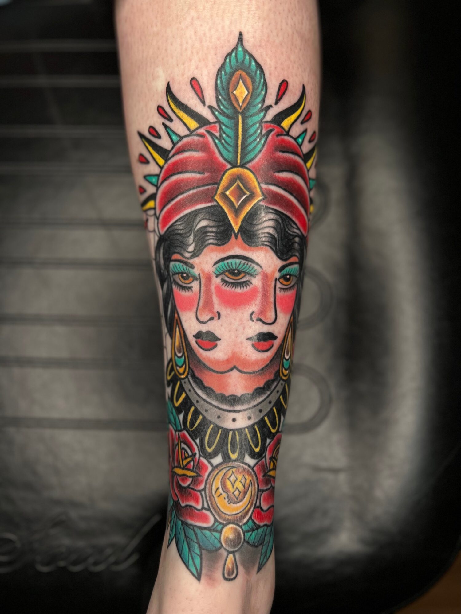 Colorful tattoo of a woman's face with elaborate headdress and jewelry on a person's arm.