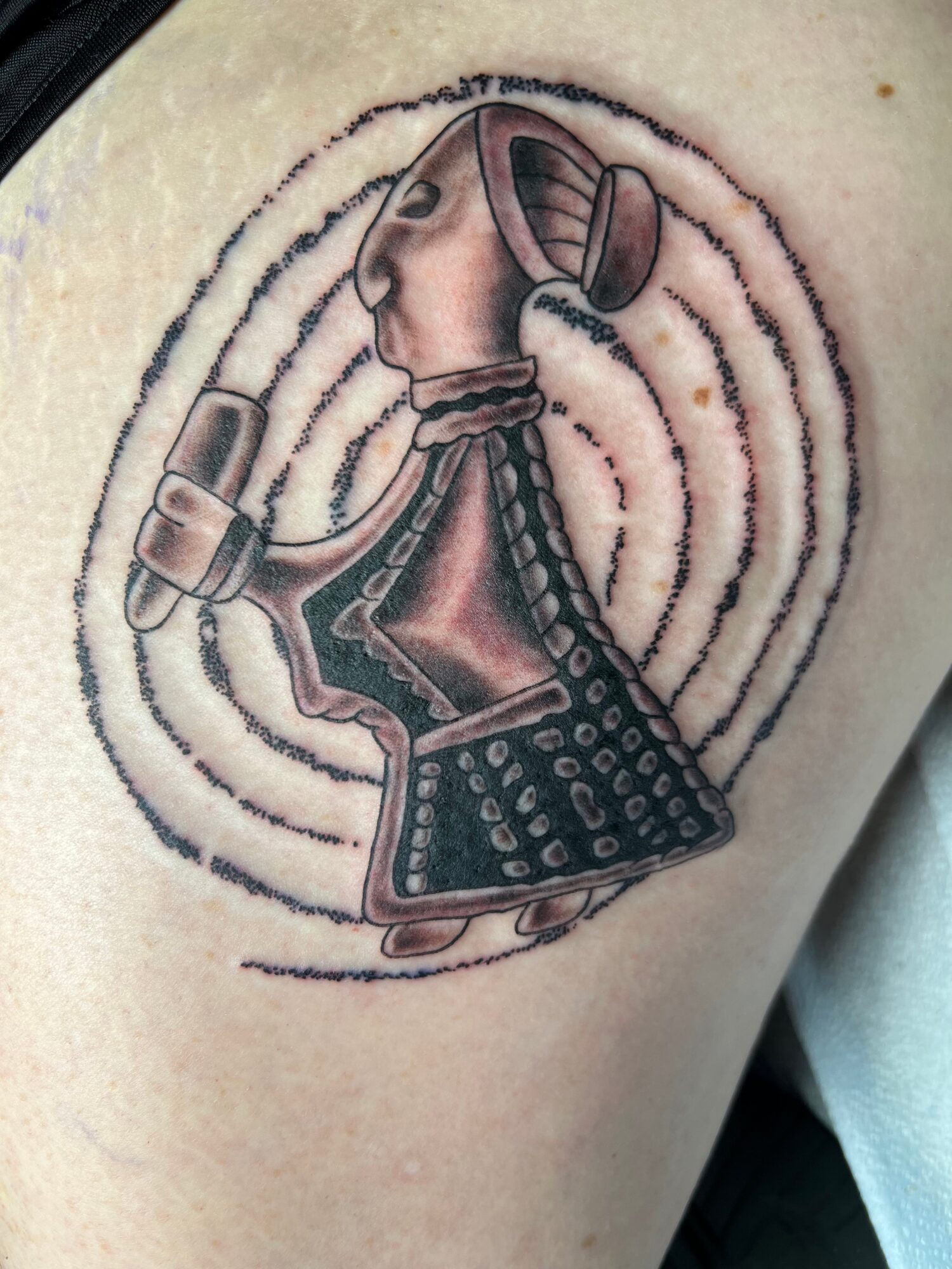 Tattoo of a person with headphones, holding a vintage radio, surrounded by concentric circles, on skin.